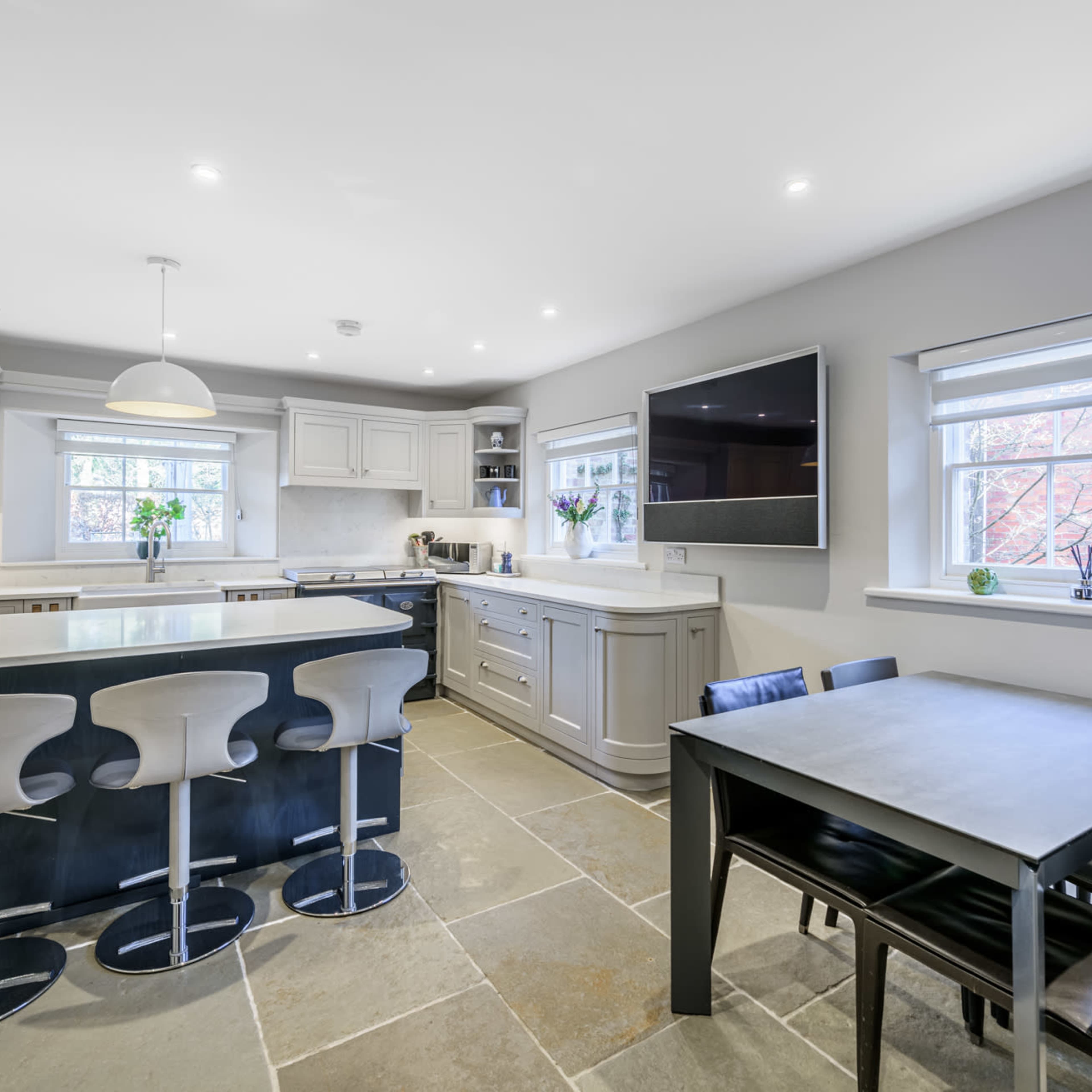A modern kitchen features gray cabinetry, a central island with bar stools, and a dining table near a window.