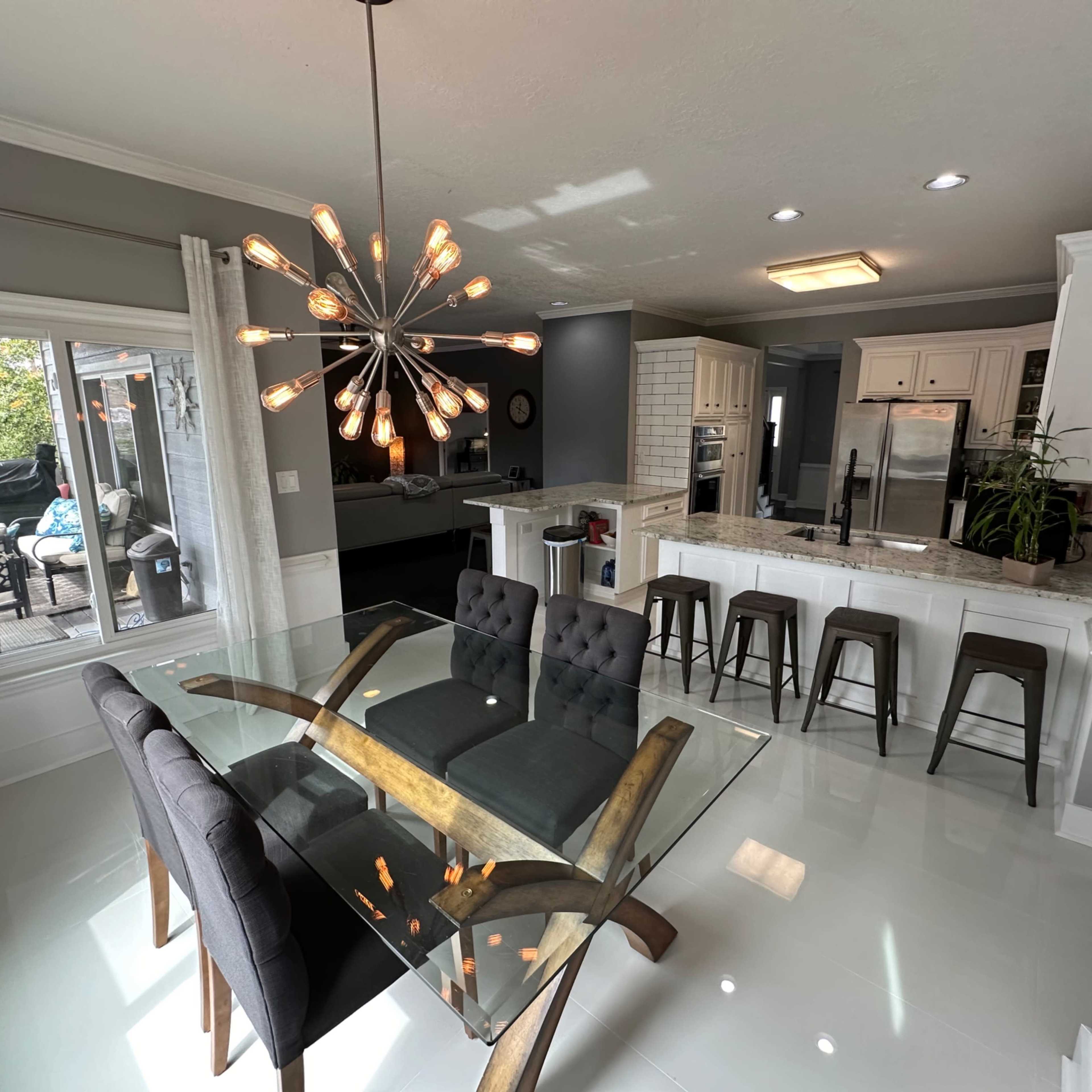 A modern kitchen features a glass dining table with upholstered chairs, a granite countertop, and stainless steel appliances.