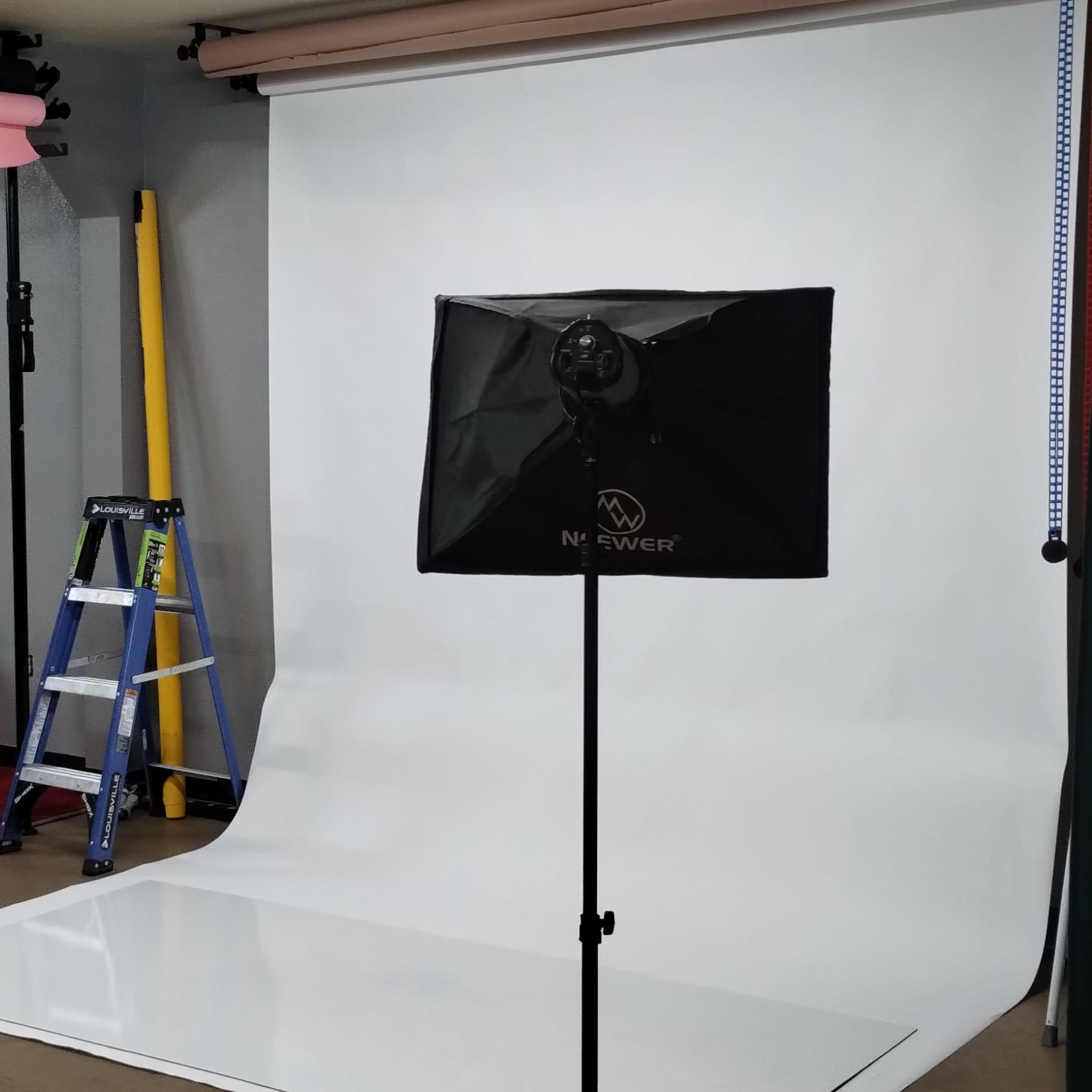 A photography studio setup with two light stands, a white backdrop, and a ladder in the background.