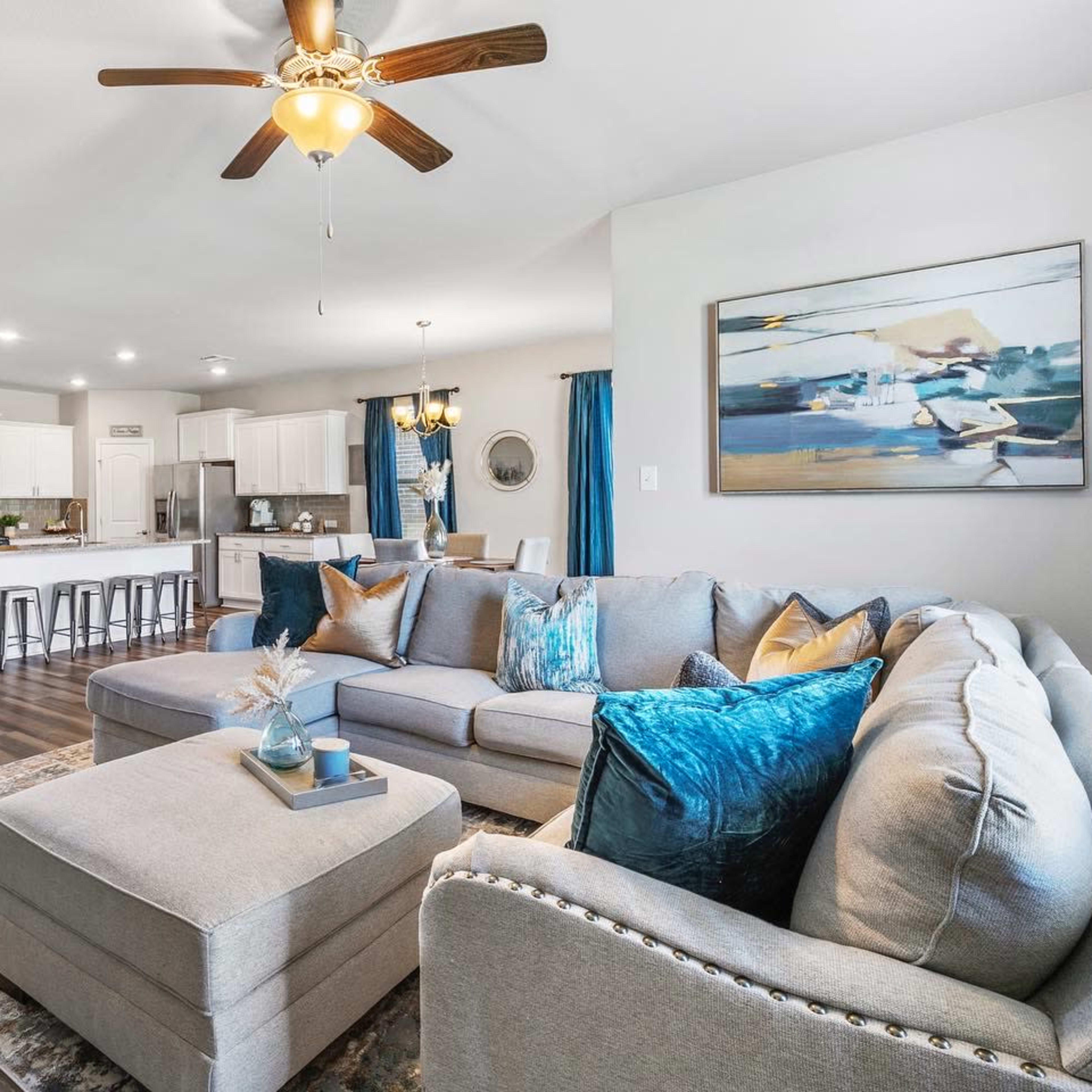 A spacious living room features a sectional sofa, a coffee table, and a view of an open kitchen with modern appliances.