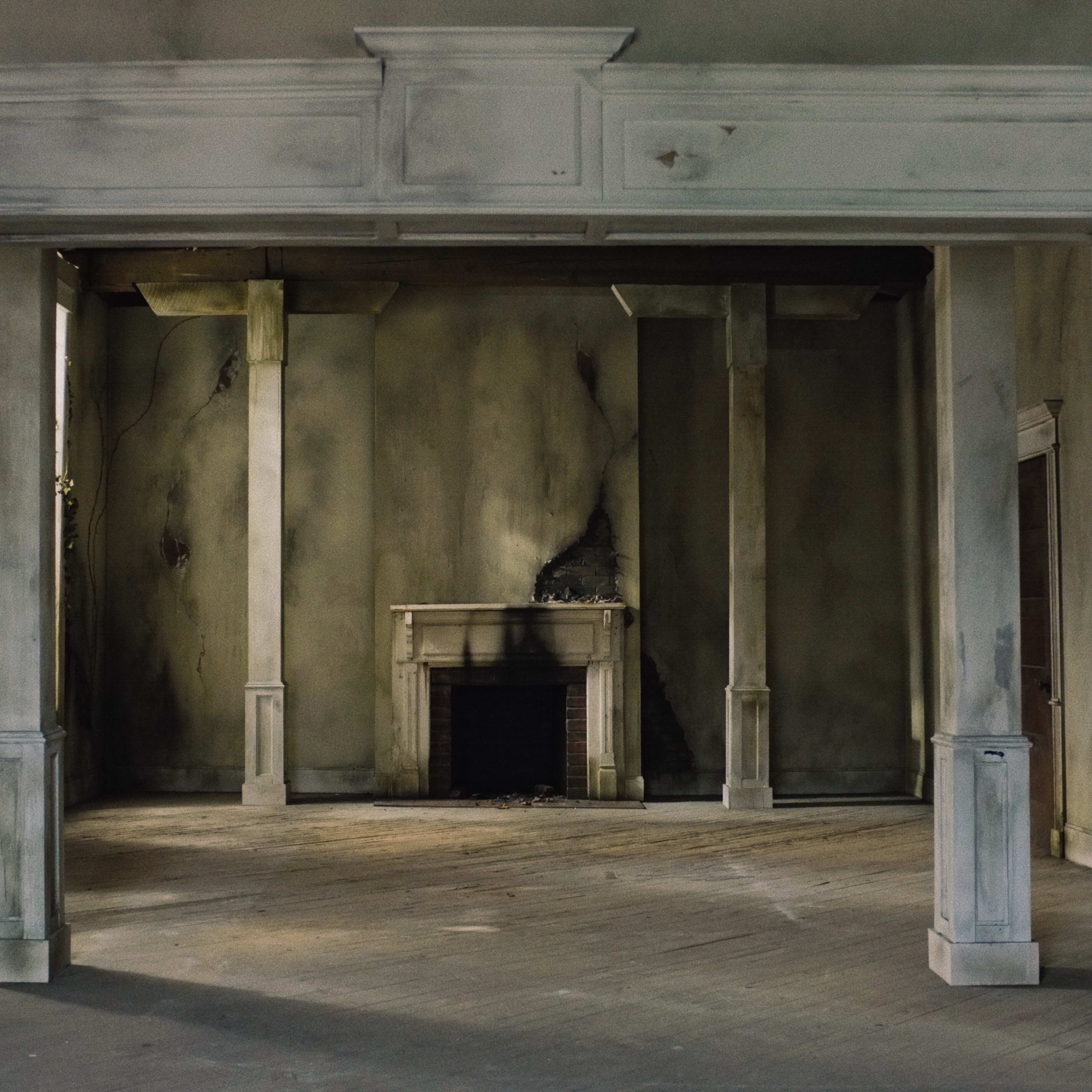 An empty and dilapidated room with a fireplace and white columns framing an entrance.