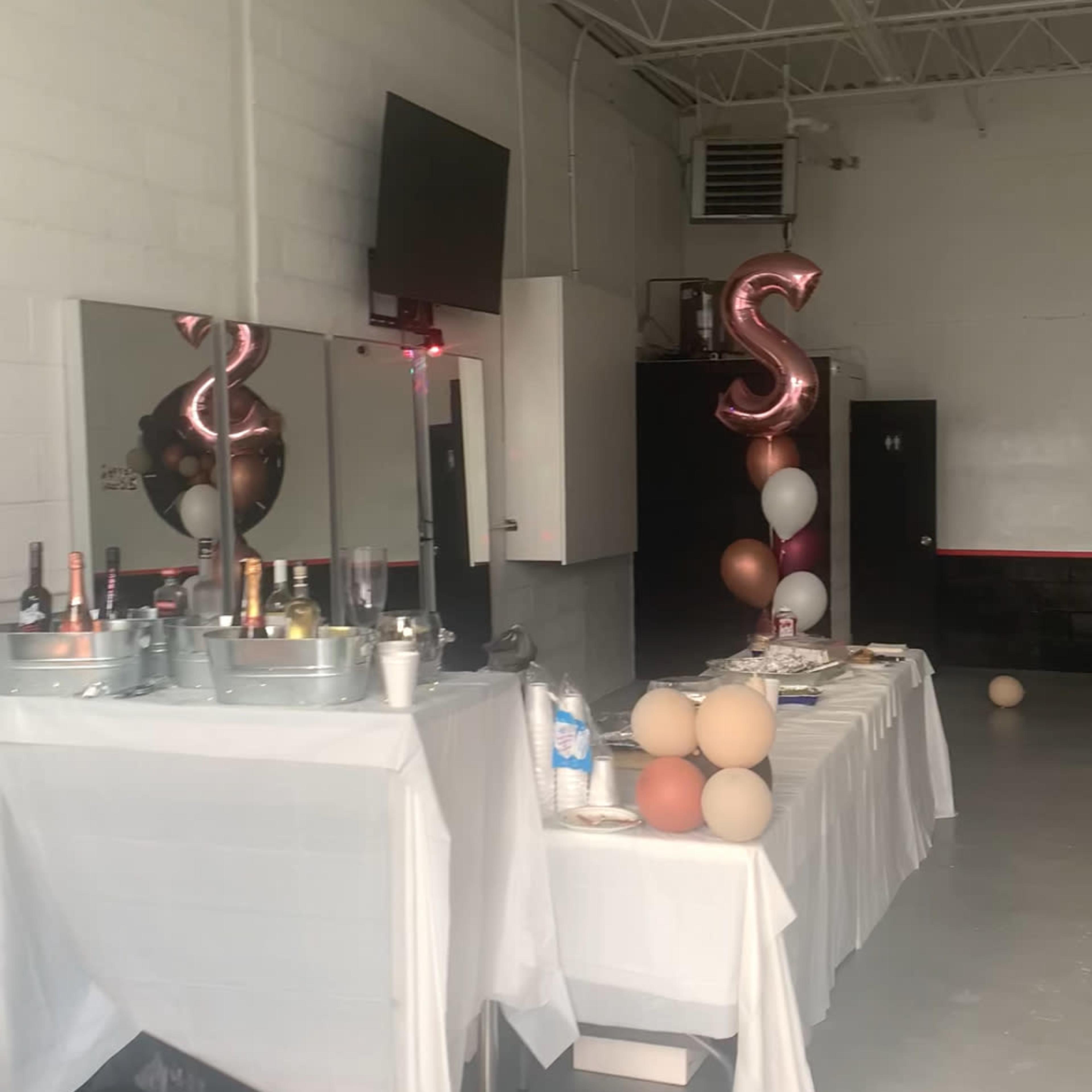 A party setup featuring a table with drinks, balloons, and a mirrored wall in a spacious room.