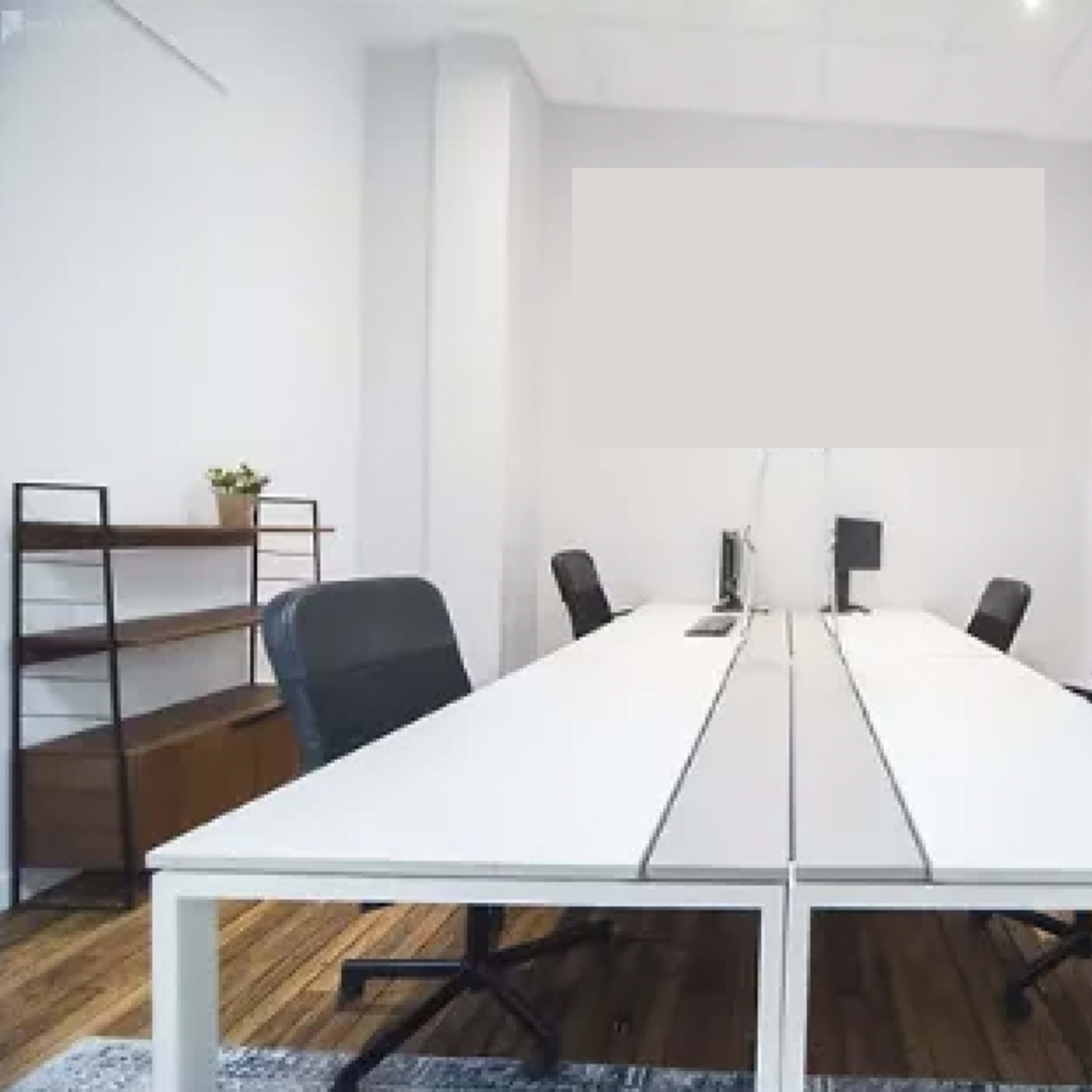 A minimalistic office space with a long white table, black chairs, and a bookshelf.