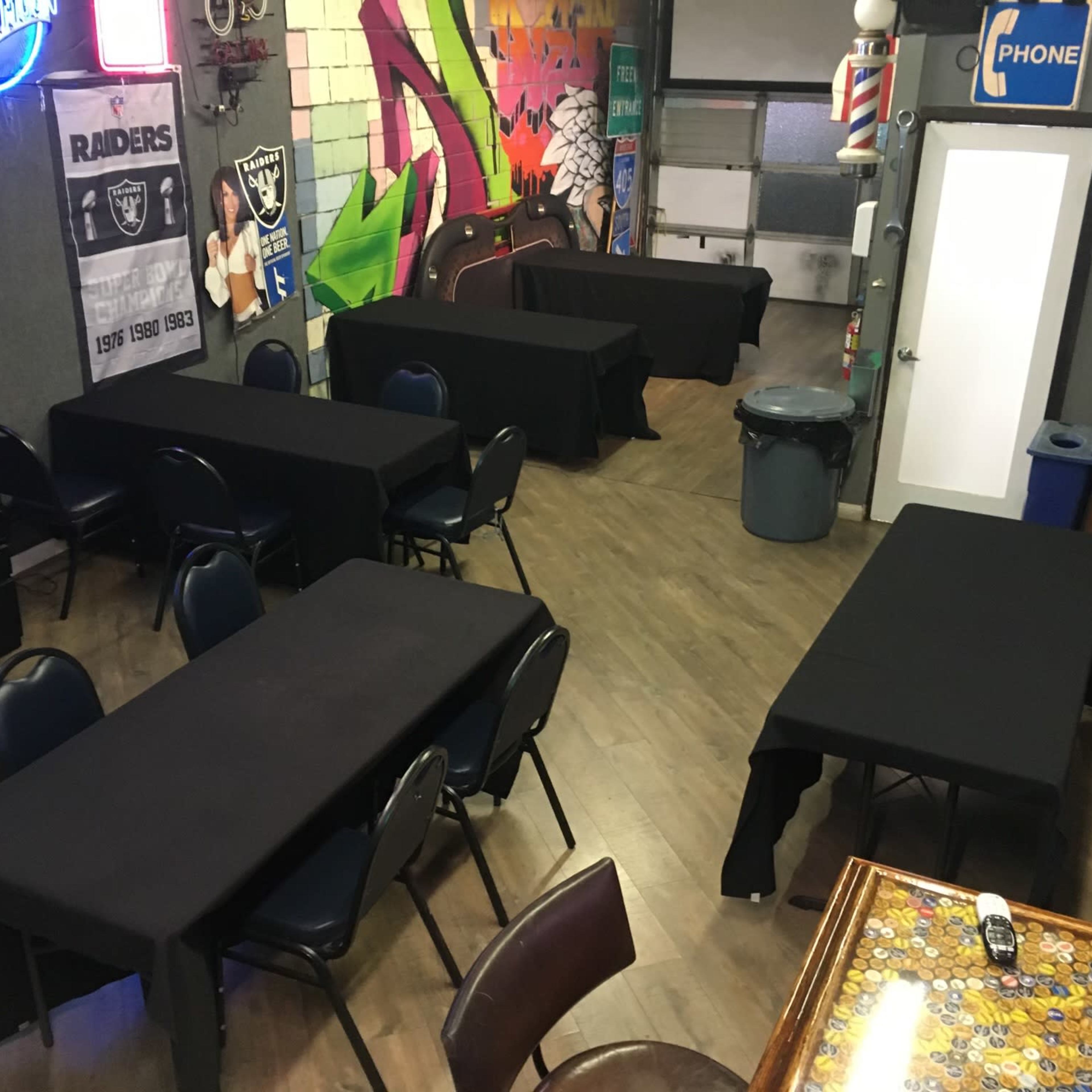 A room with several tables covered in black cloth, surrounded by chairs, and decorated with a mural and colorful signage.