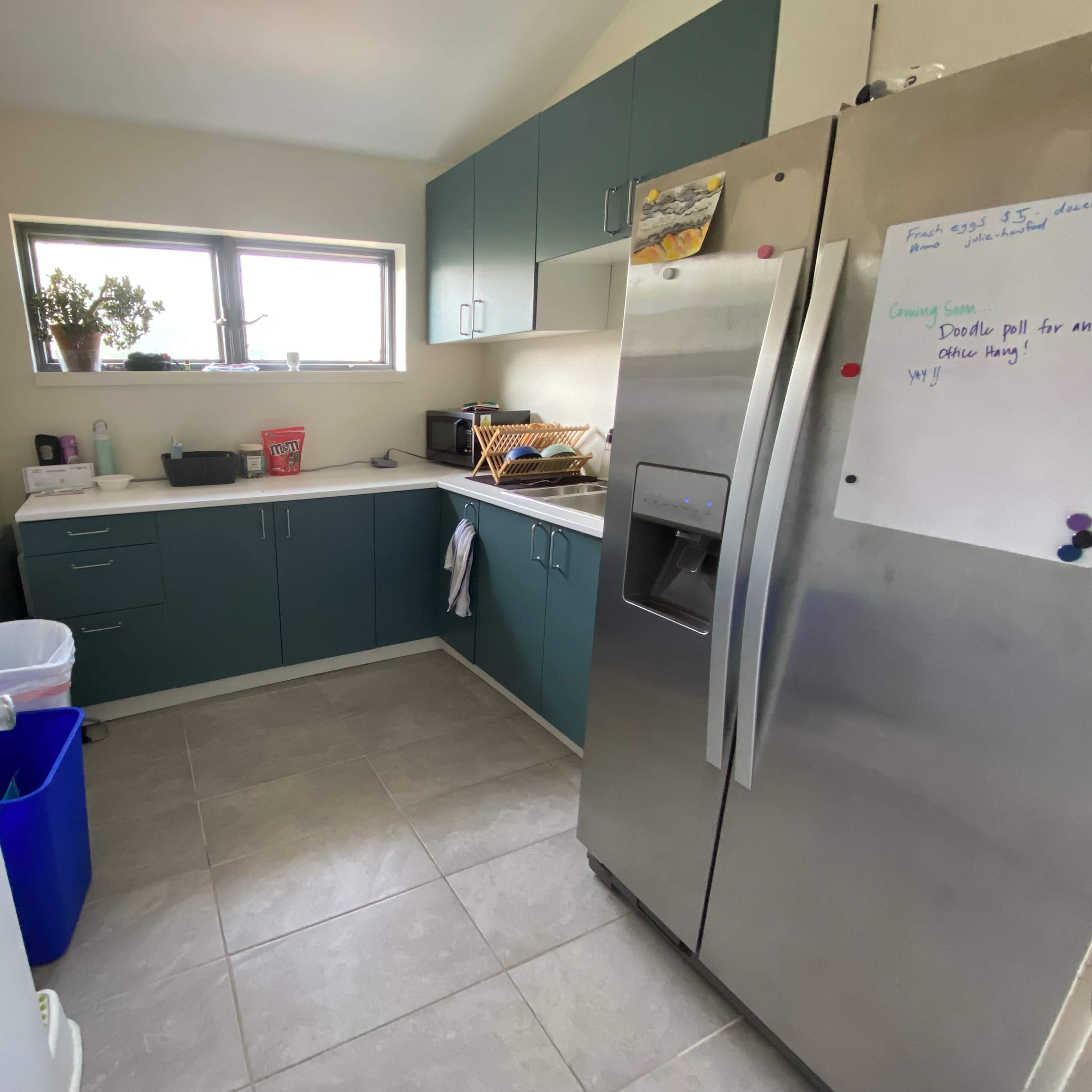 A small kitchen featuring teal cabinets, a stainless steel refrigerator, and a countertop with various kitchen items.