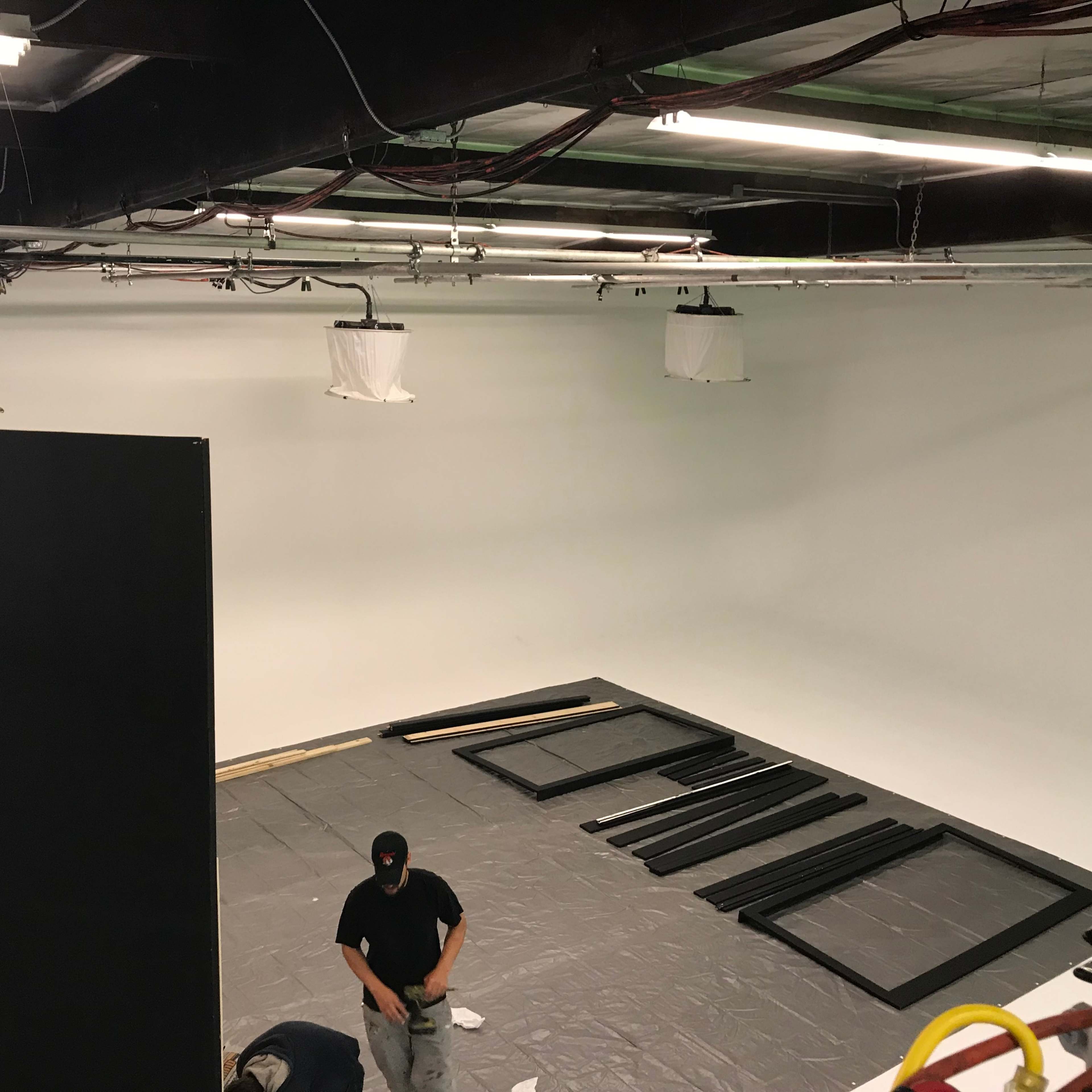 Two individuals are assembling equipment in a spacious studio with a white backdrop.