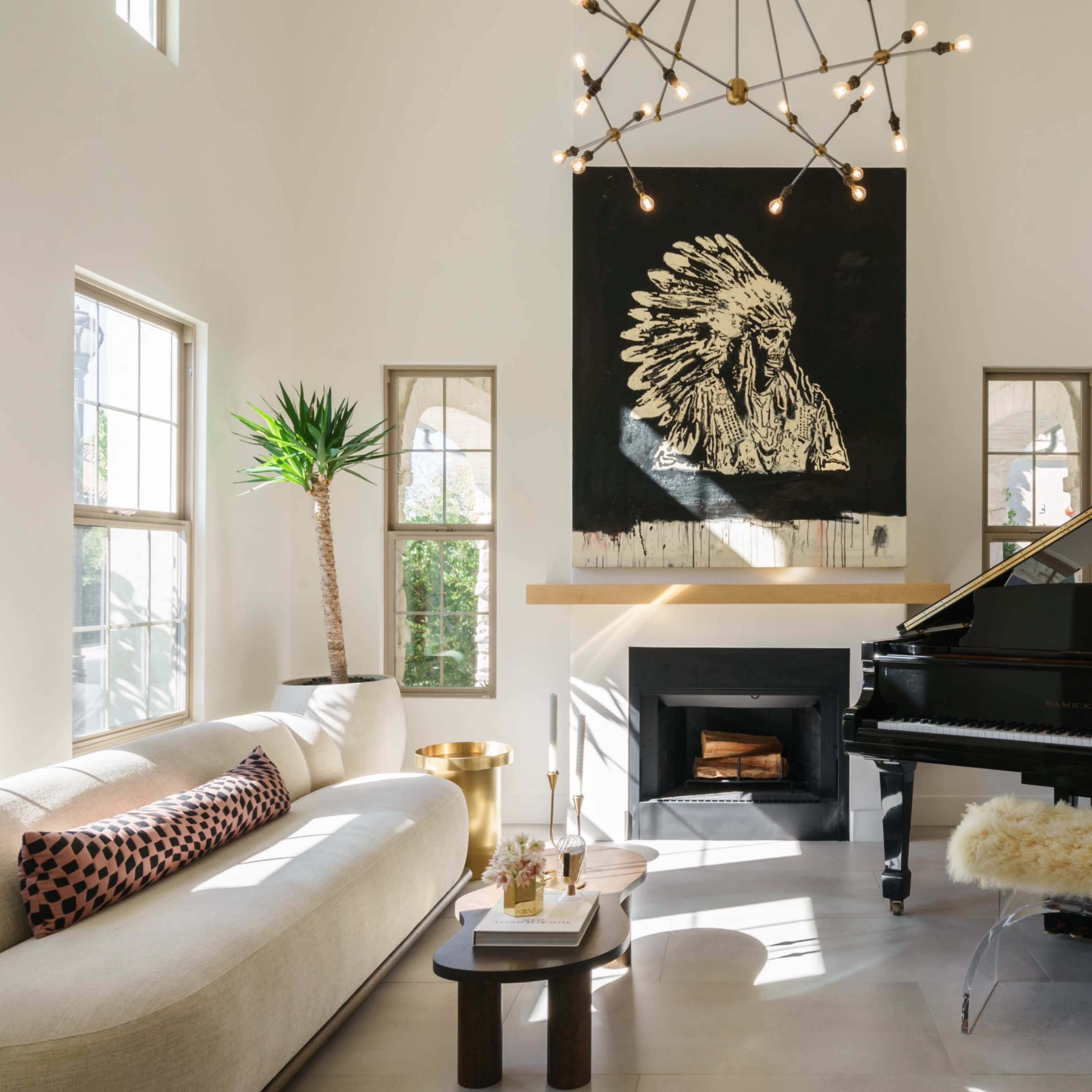 This living room features a grand piano, a large artwork of a native chief, and a modern sectional sofa under a chandelier.