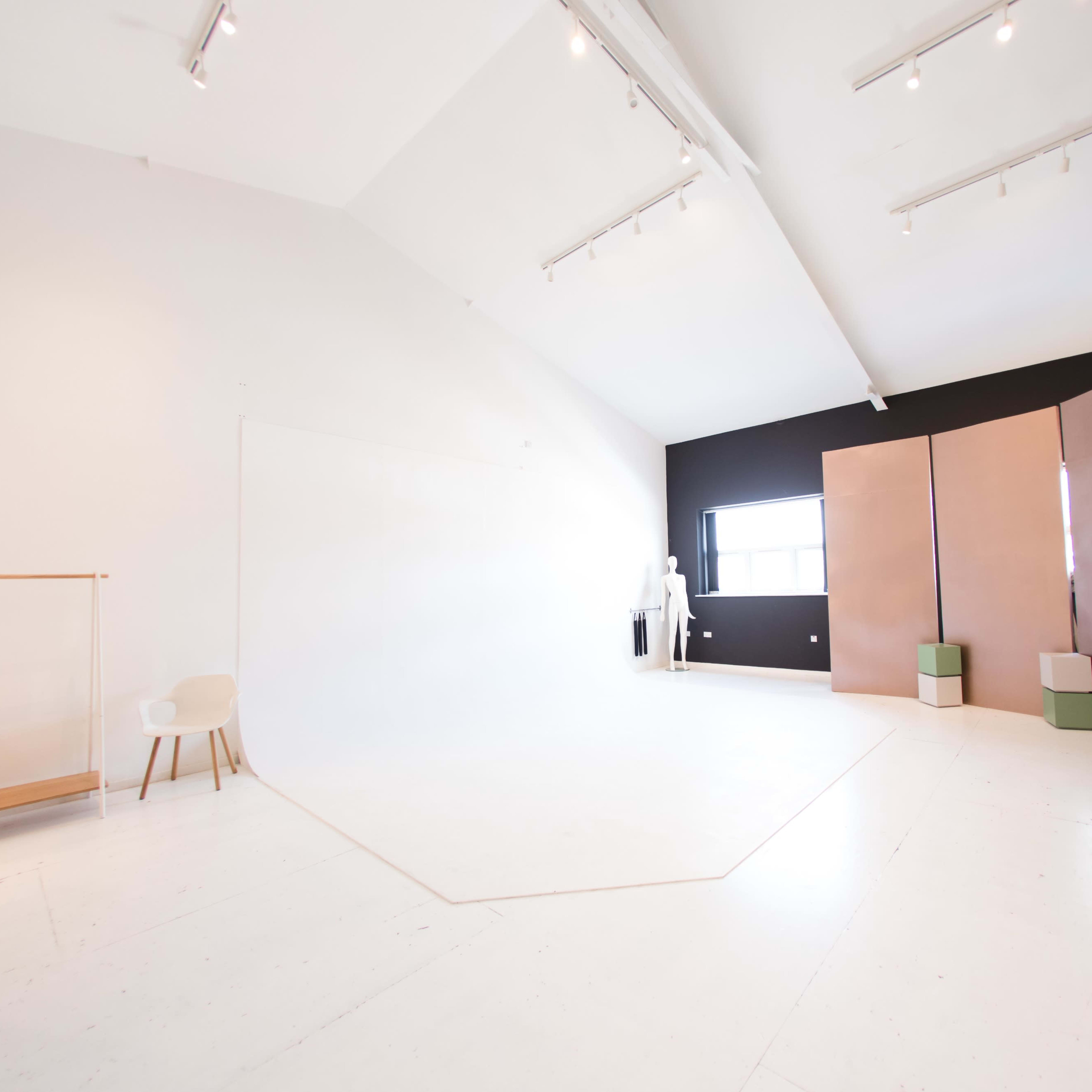 A spacious photography studio with white walls, a black accent wall, and several geometric backdrops arranged in the corner.