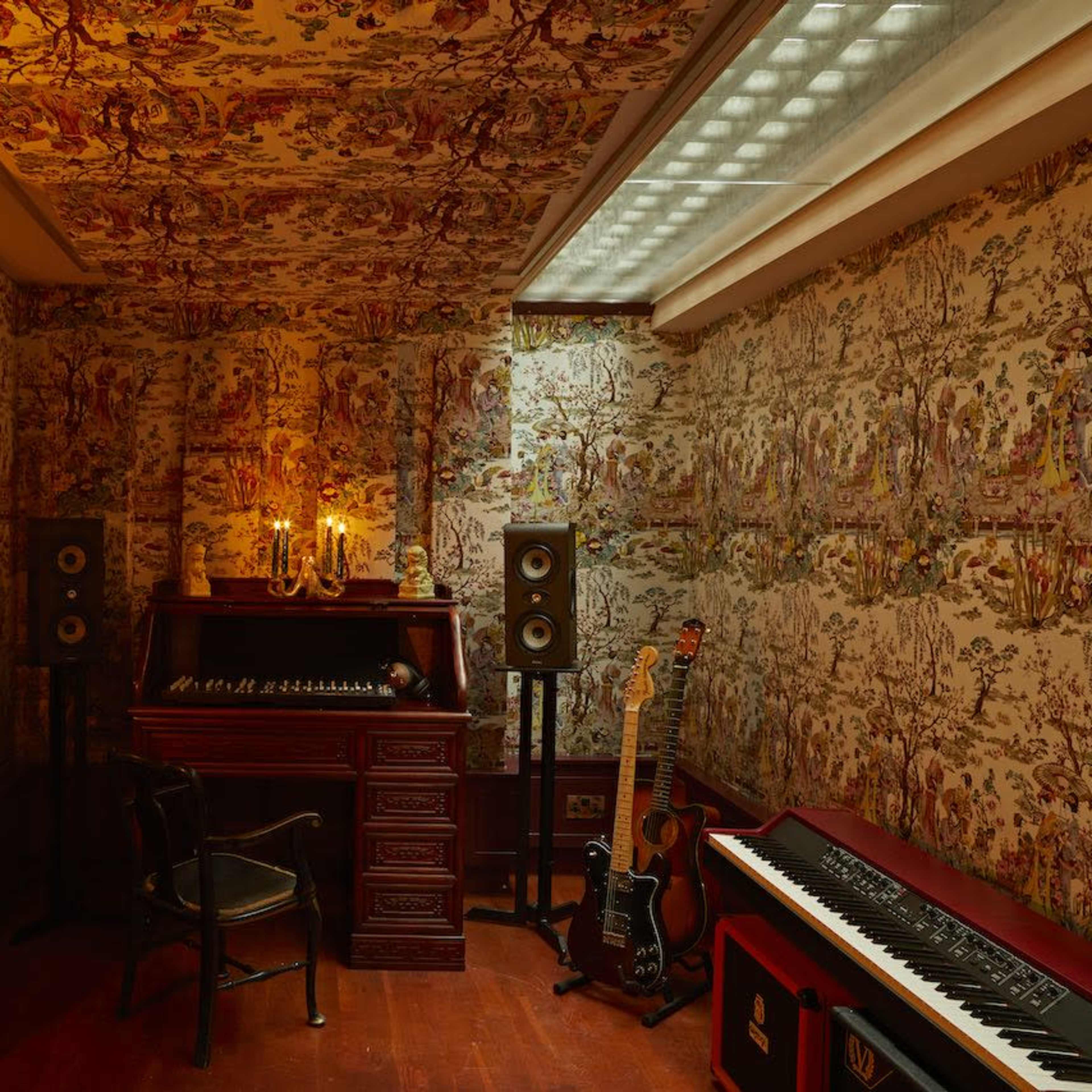 A cozy room features ornate floral wallpaper, a vintage organ, and music equipment, illuminated by soft candlelight.