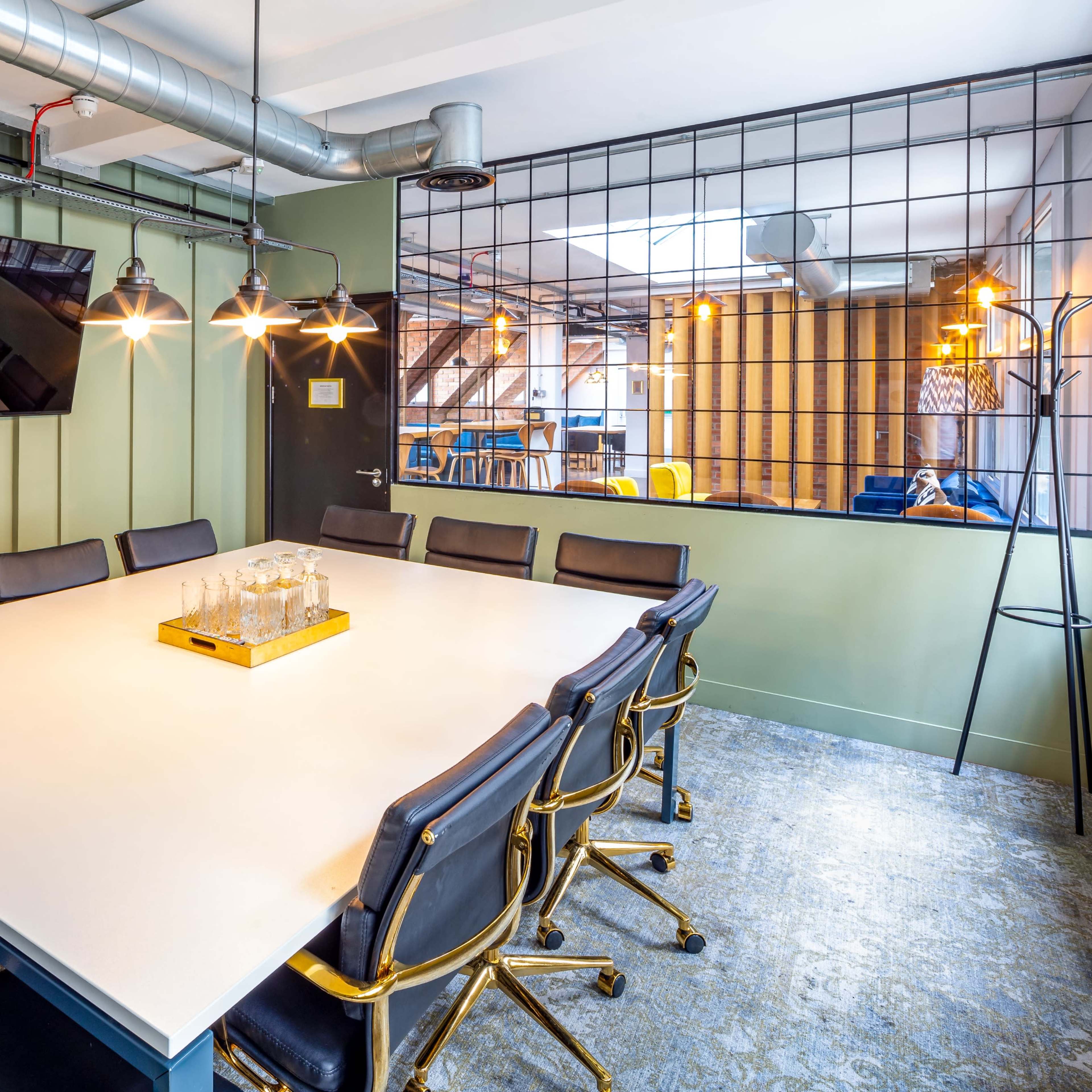A modern conference room with a large white table surrounded by black office chairs, a television mounted on the wall, and industrial-style lighting fixtures.