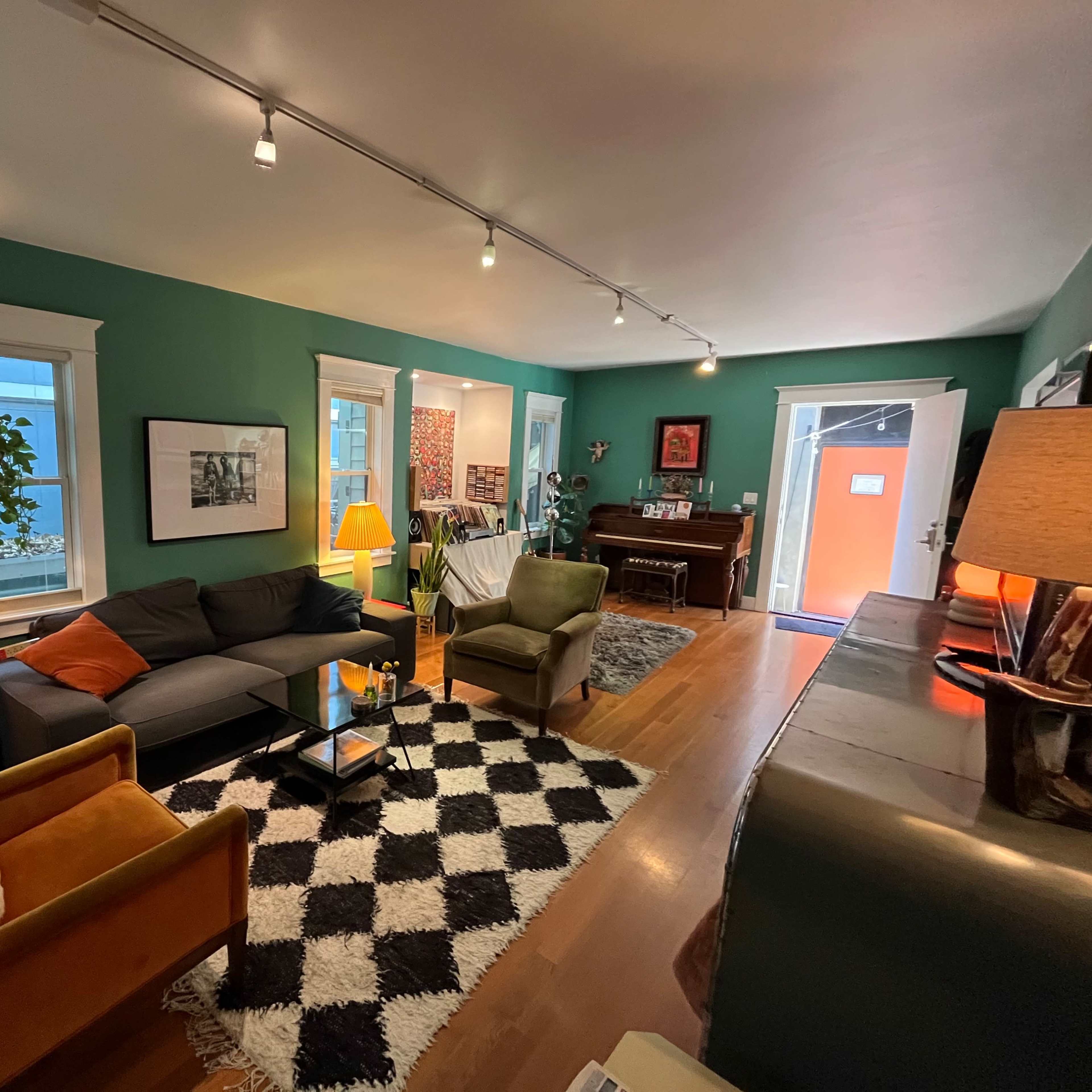 The room features a green-painted interior with a gray couch, black and white rug, and various decorative furniture, including an orange accent chair and a console table.