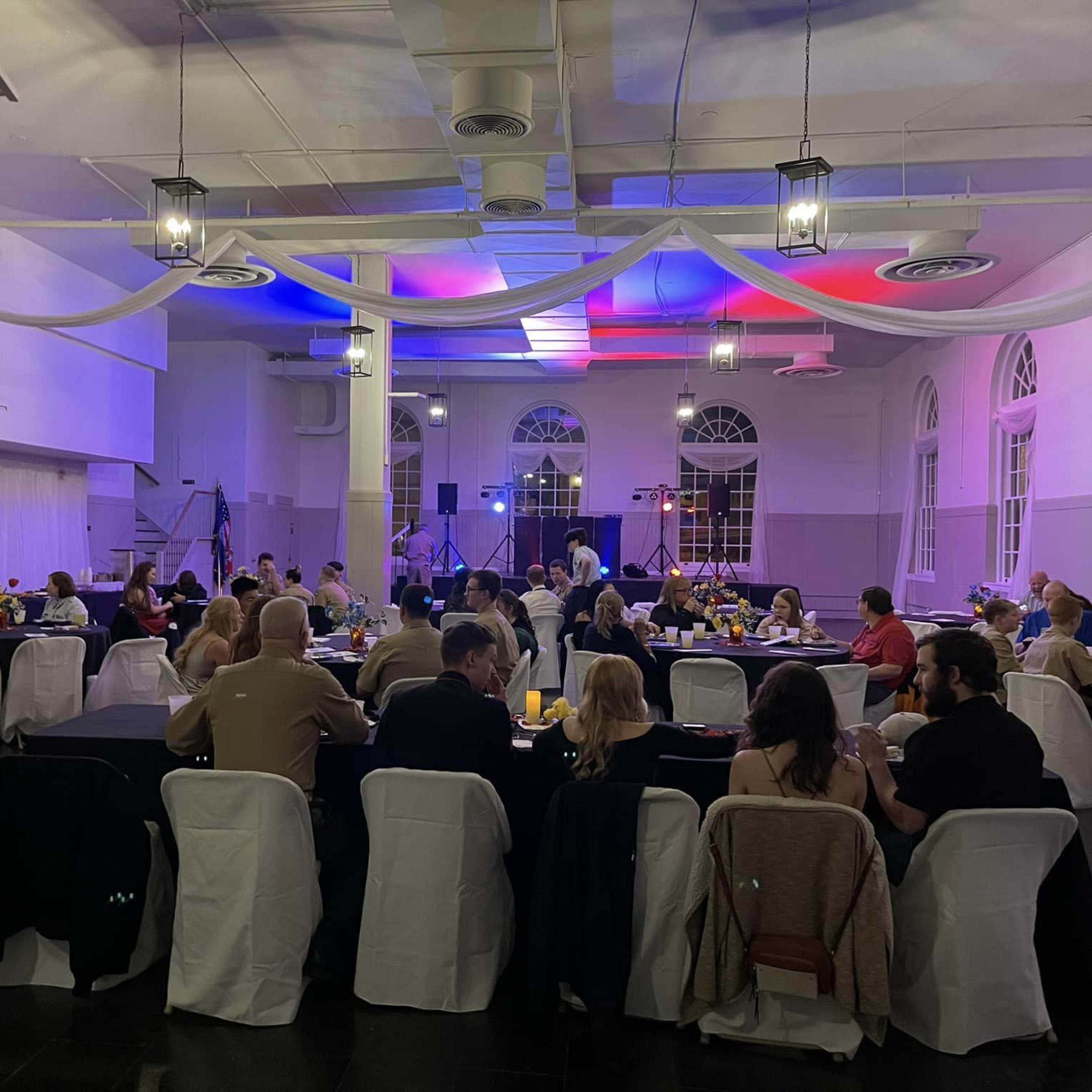A banquet hall filled with guests seated at tables, with decorations and lighting creating a festive atmosphere.