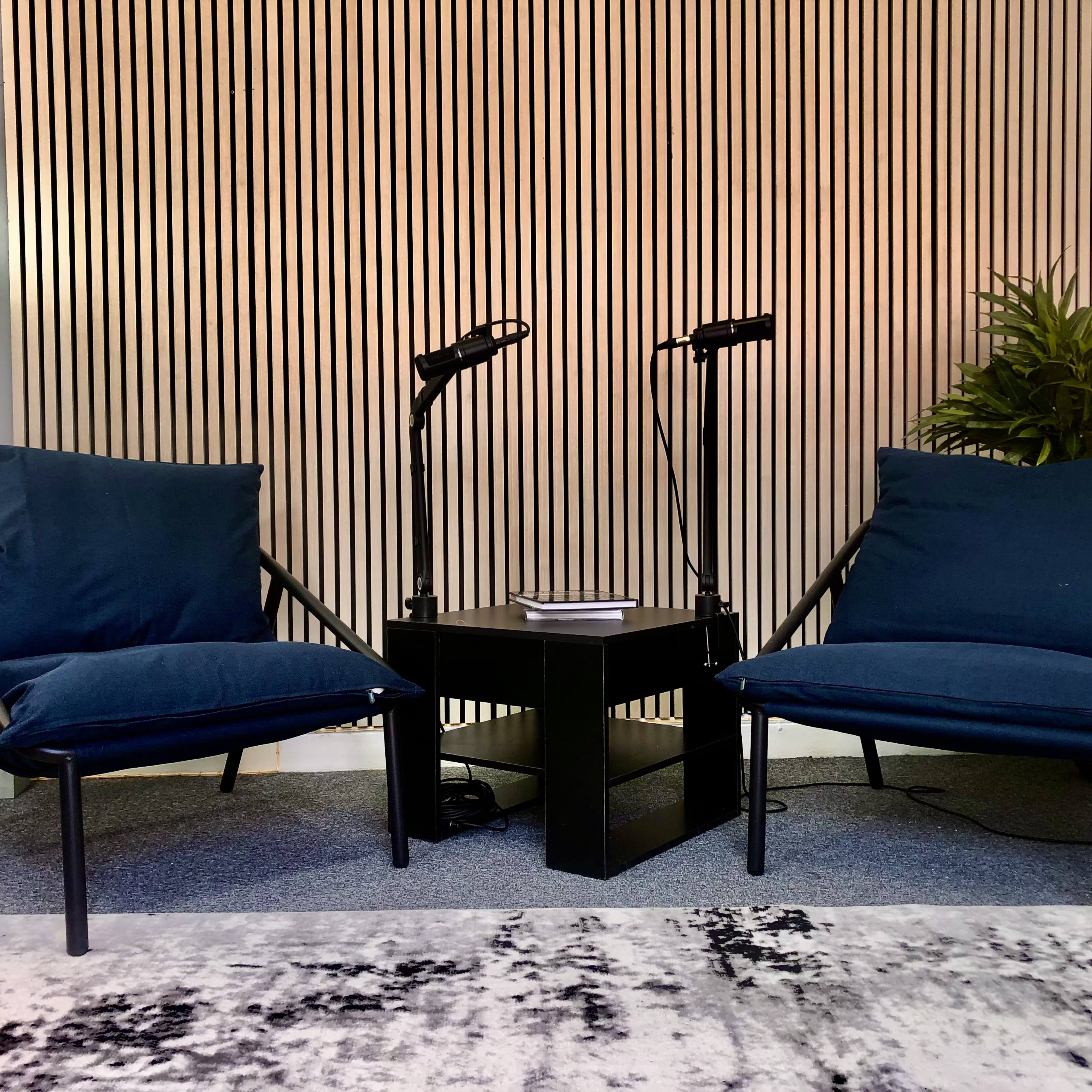 Two navy blue chairs facing each other around a black table, with a potted plant and lamps in the background against a striped wall.