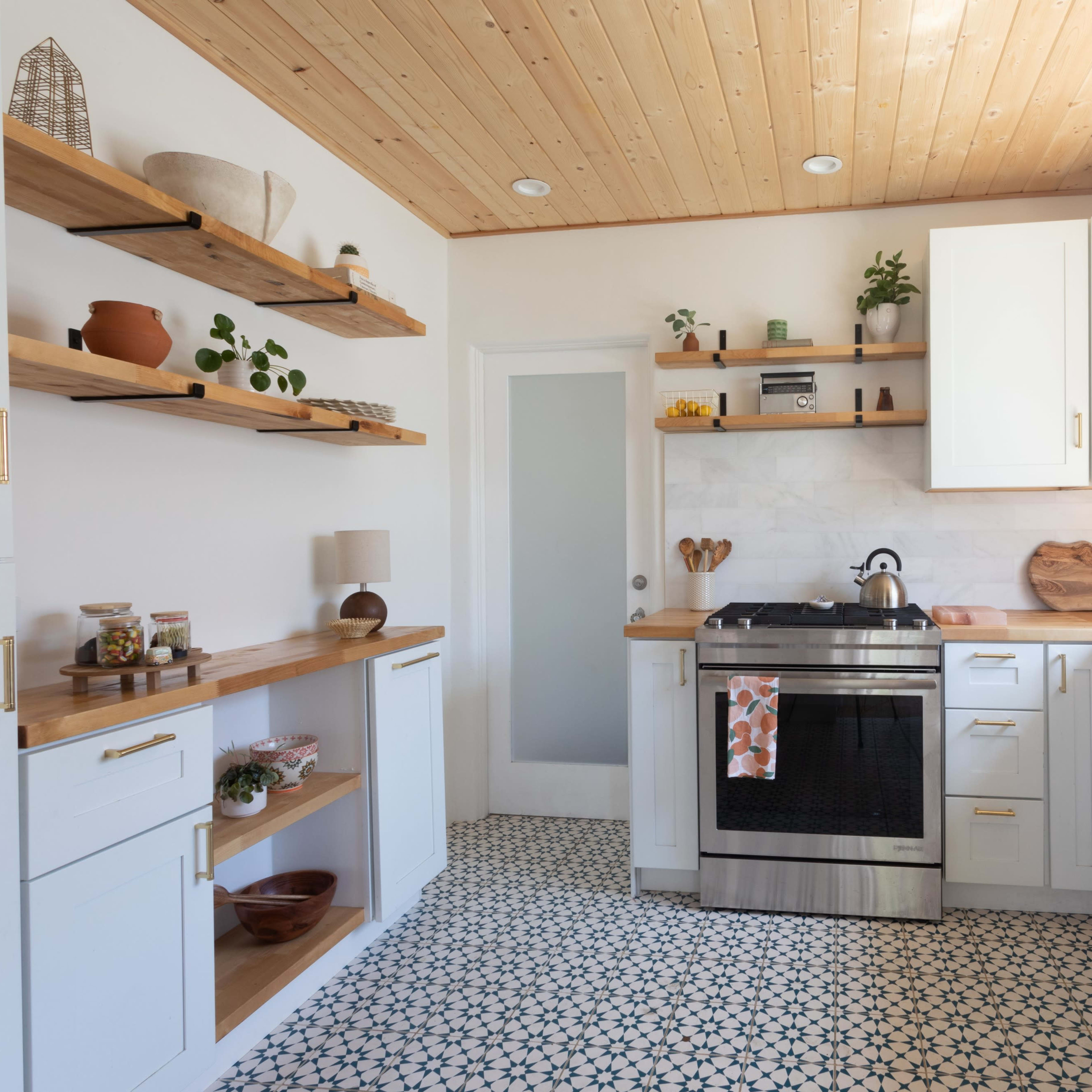A modern kitchen with white cabinets, open shelves, a stainless steel stove, and a patterned tile floor.