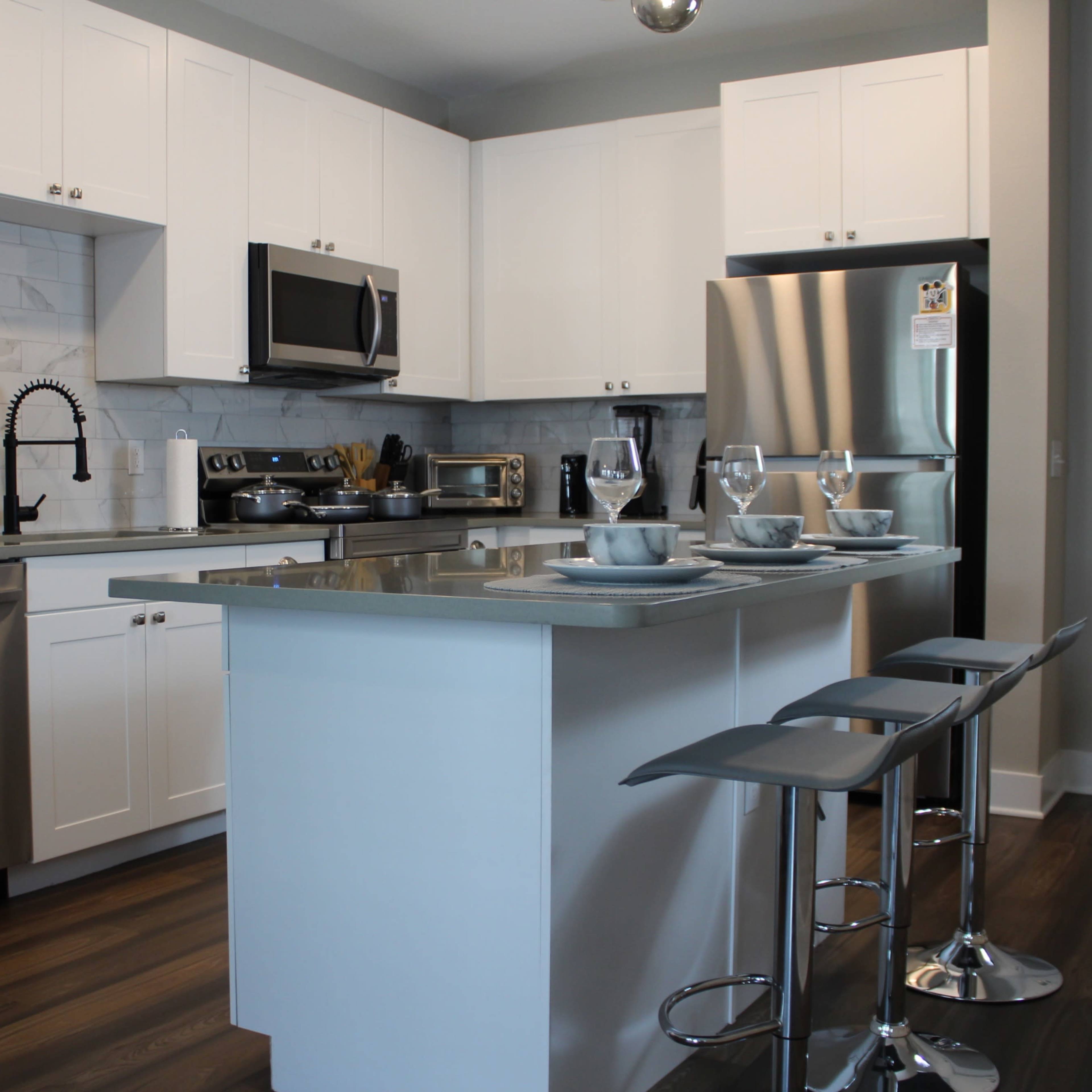 A modern kitchen with white cabinetry, stainless steel appliances, a central island, and bar stools.
