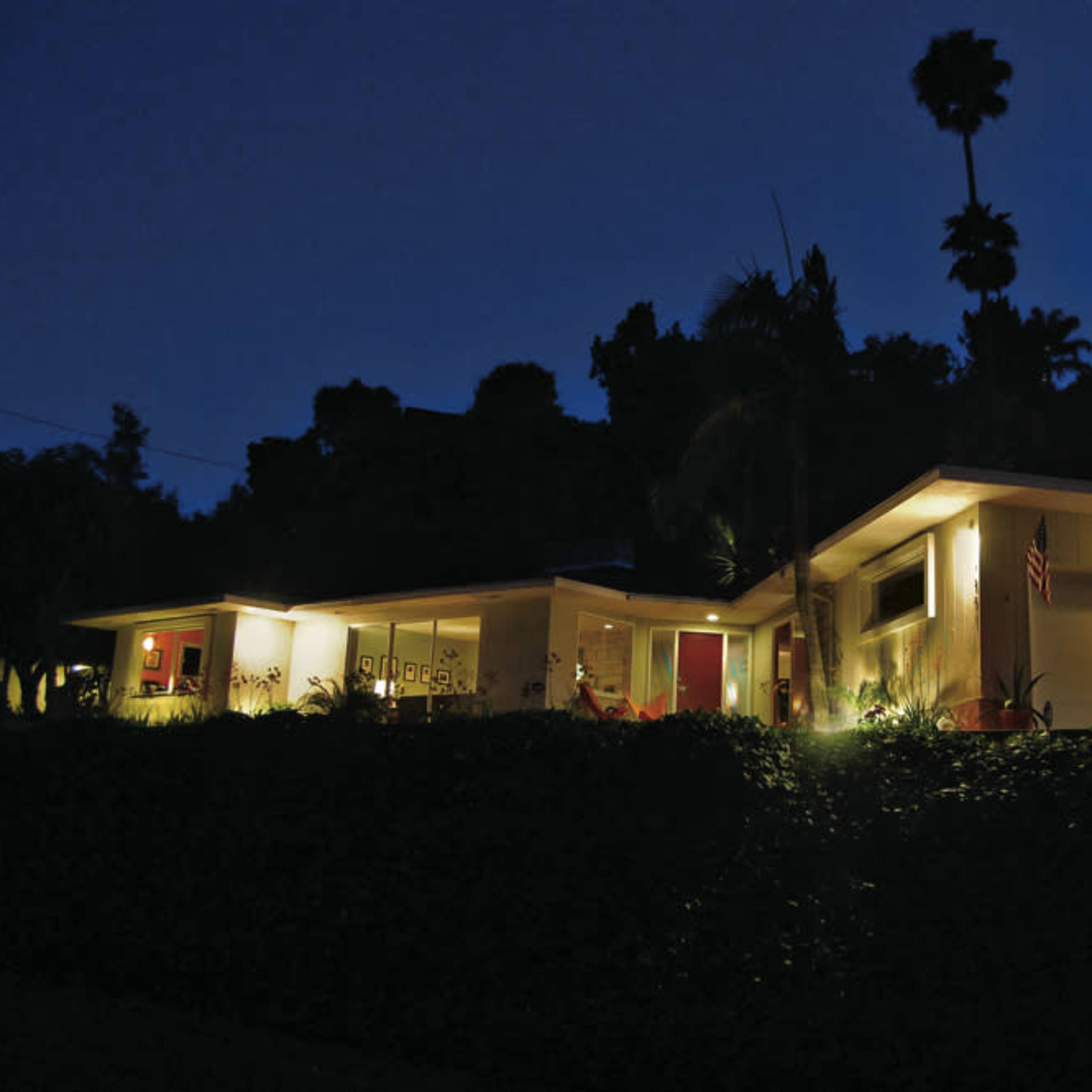 A modern house is illuminated at night, showcasing its architectural design and landscaped surroundings.