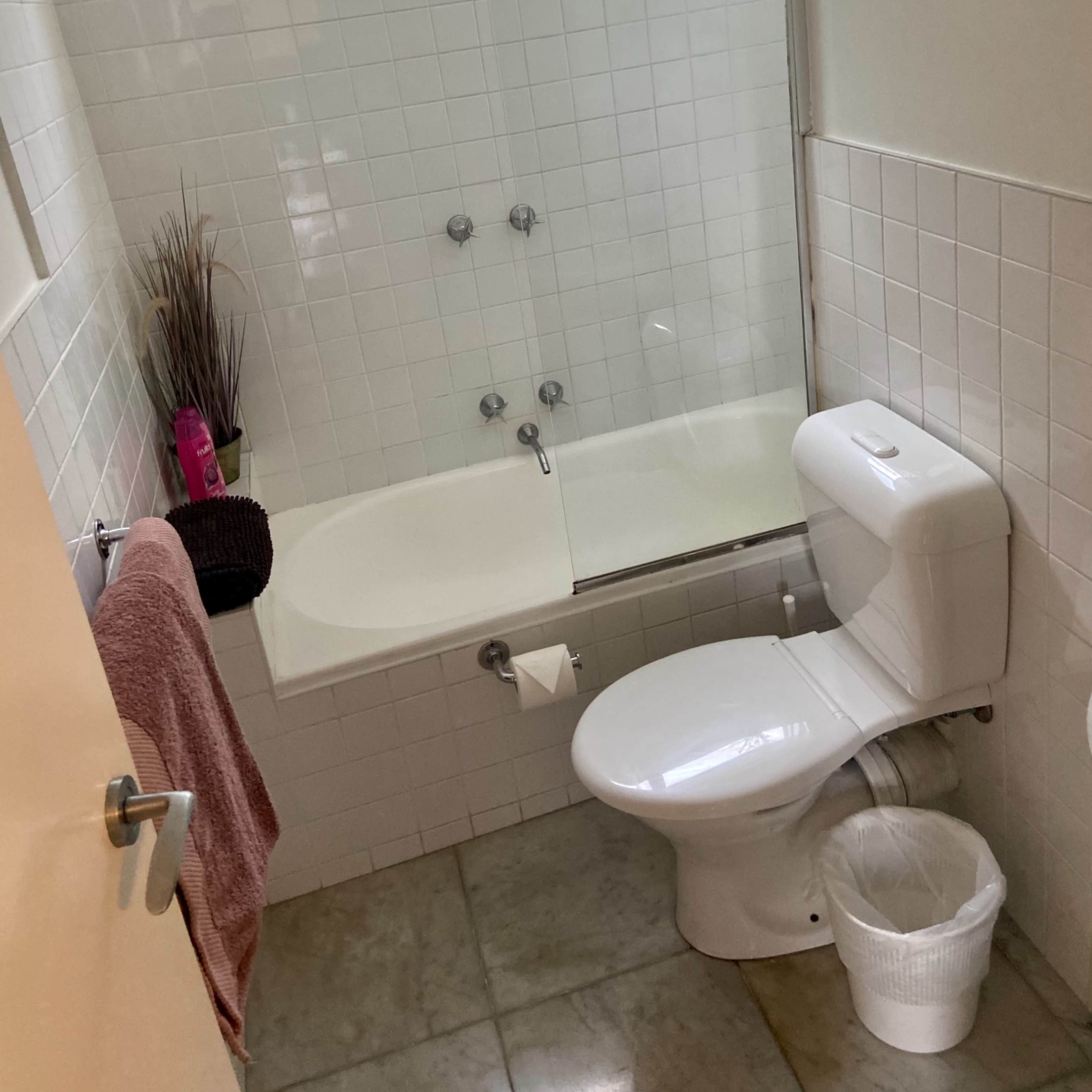 A small bathroom with a bathtub, toilet, and a window, featuring tiled walls and a plant on the windowsill.