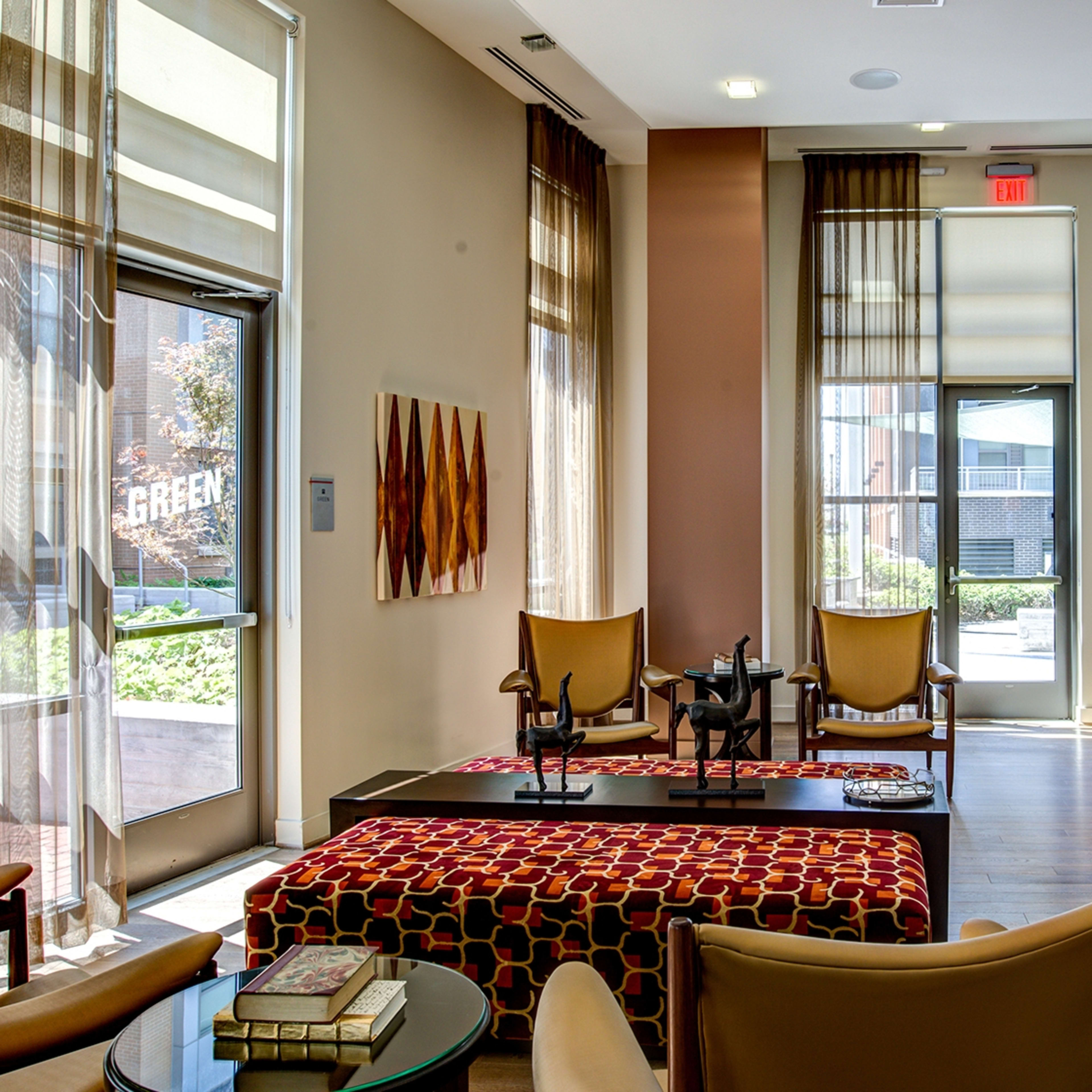 A modern lounge area with large windows, comfortable seating, and a coffee table, complemented by colorful artwork on the walls.