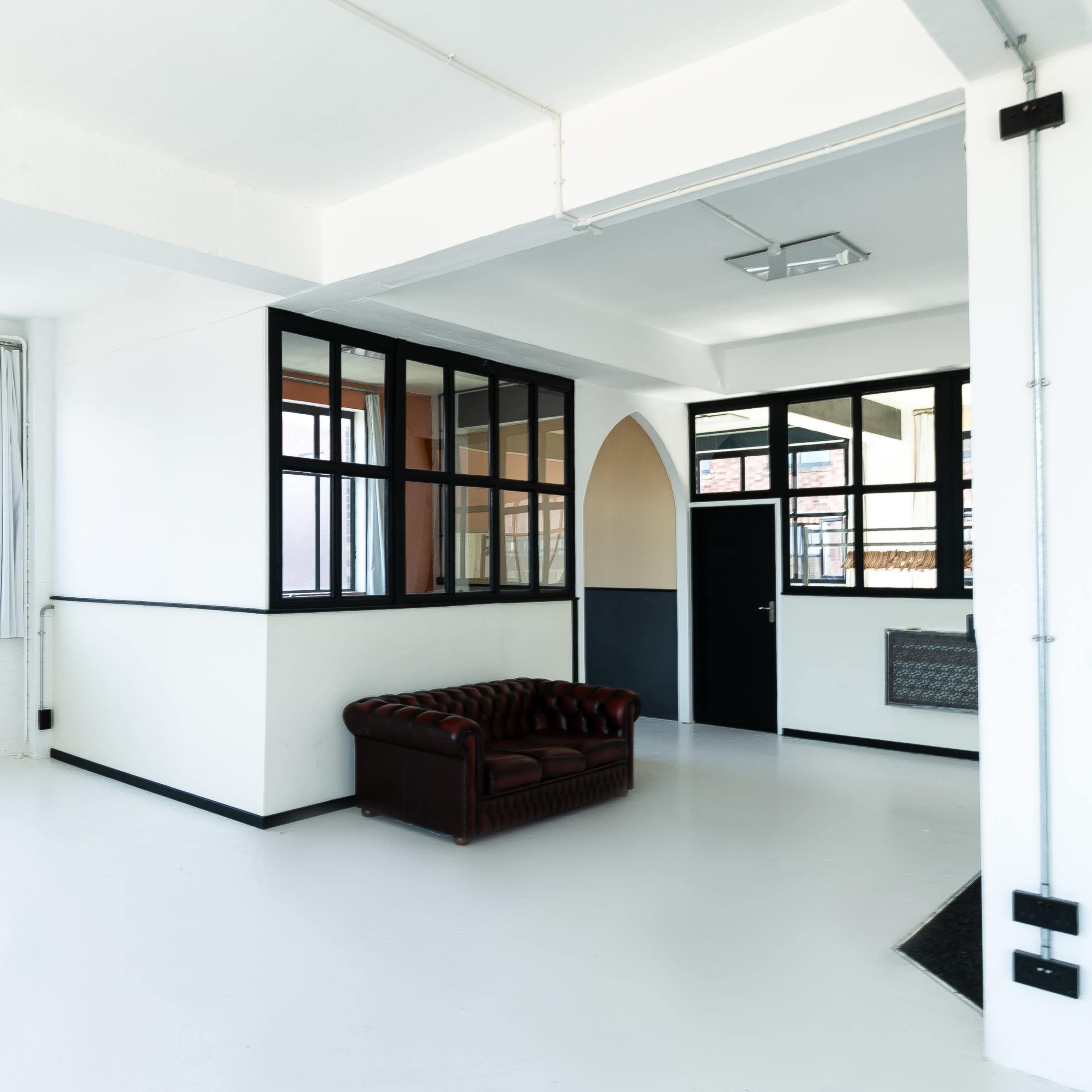 A spacious, modern room with white walls, large windows, and a brown leather sofa.