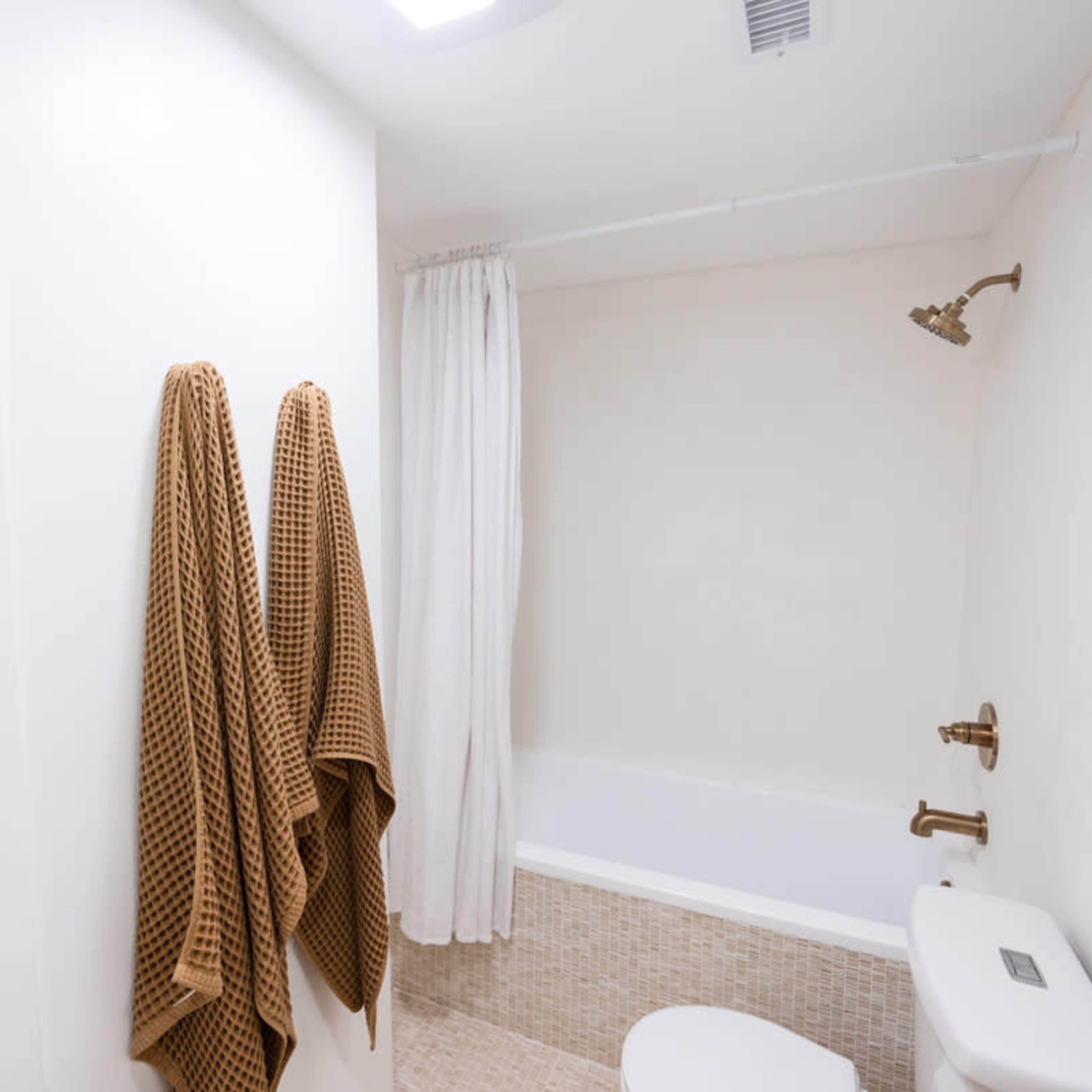 A clean bathroom with a bathtub, a showerhead, and two brown towels hanging on the wall.