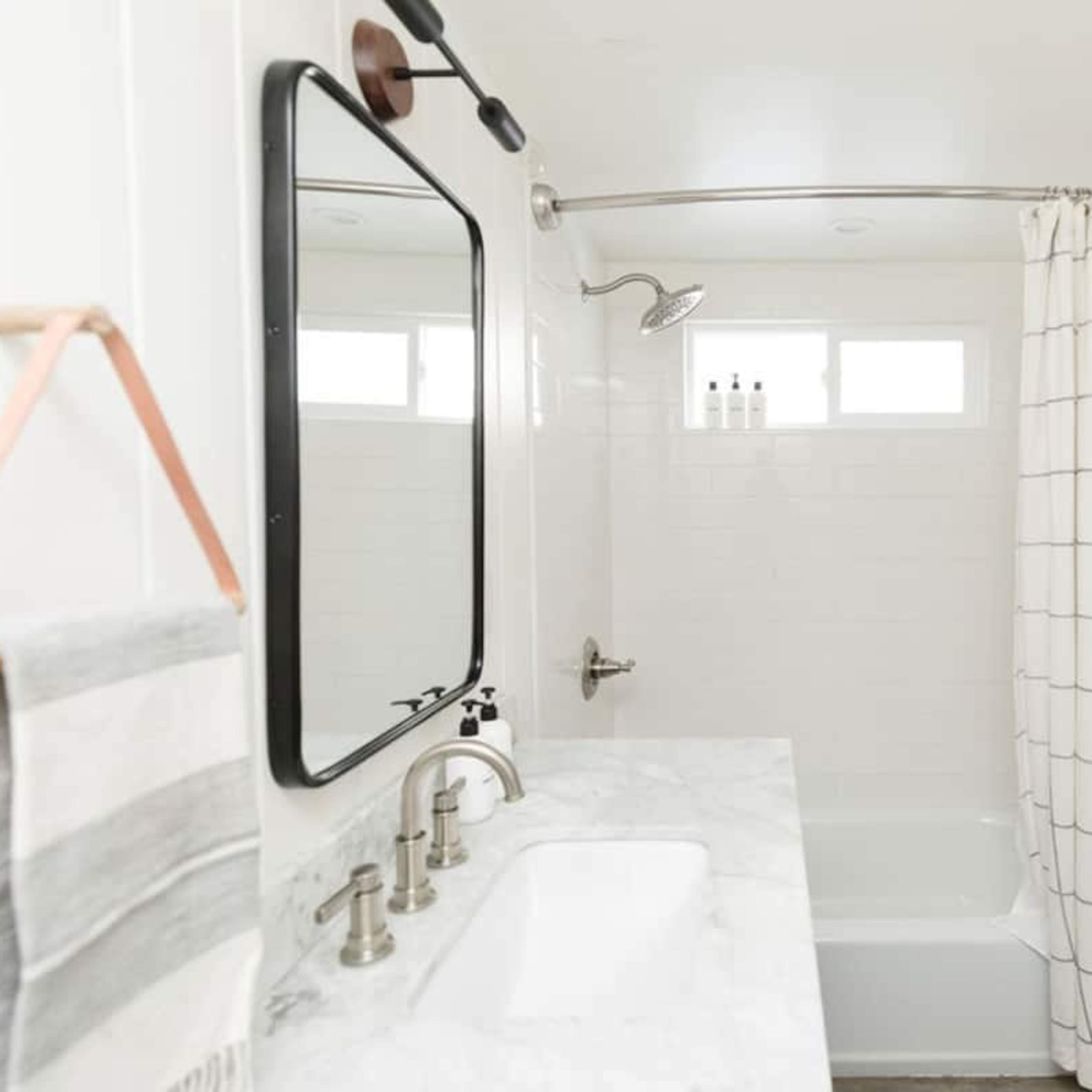 A well-lit bathroom featuring a bathtub with a shower curtain, a large mirror, and a marble countertop with faucets.