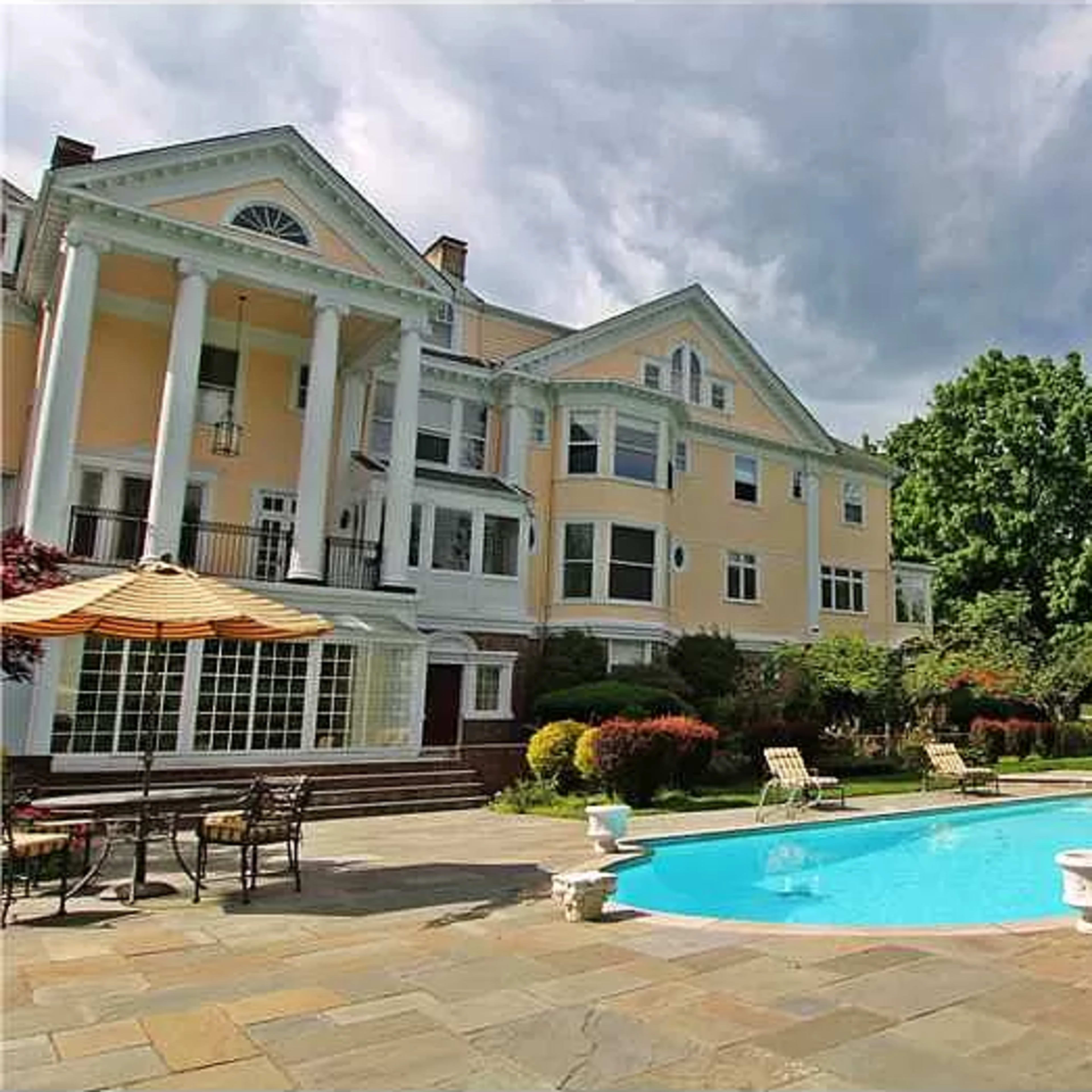 A large, elegant house with a pool surrounded by stone paving and landscaped gardens.