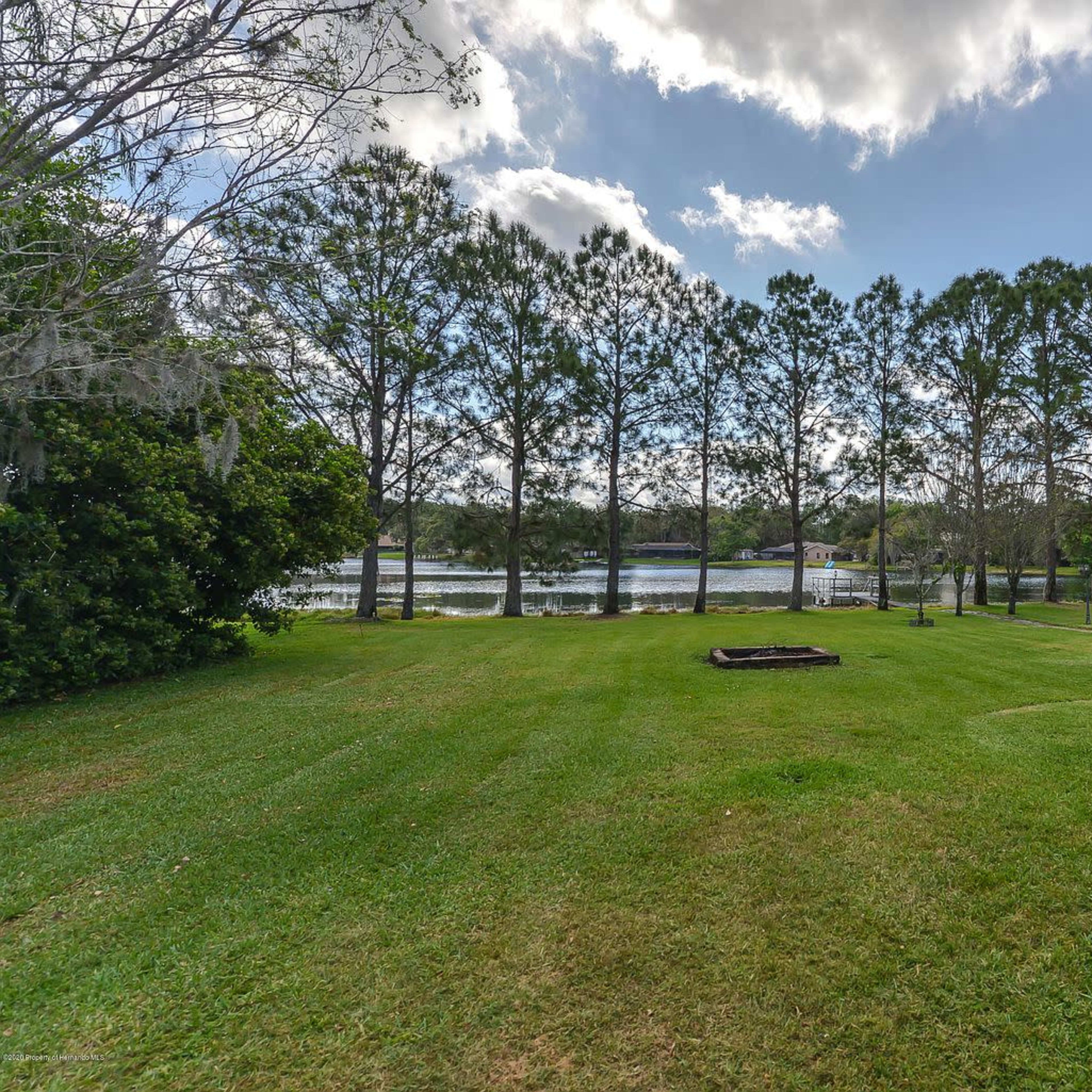 A grassy yard with a view of a lake in the background, bordered by a row of trees on one side.