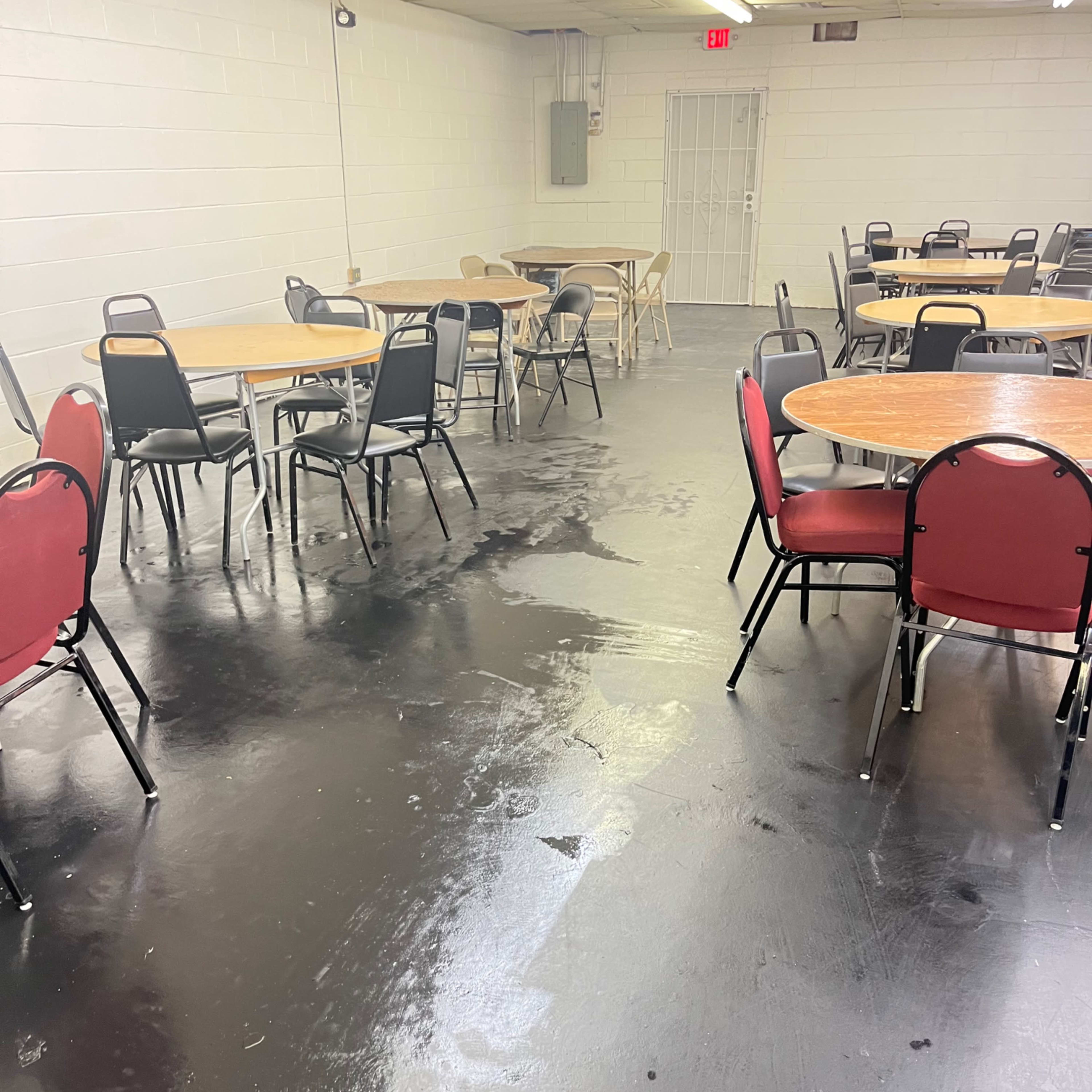 An empty room with several round tables and chairs arranged around a polished black floor.