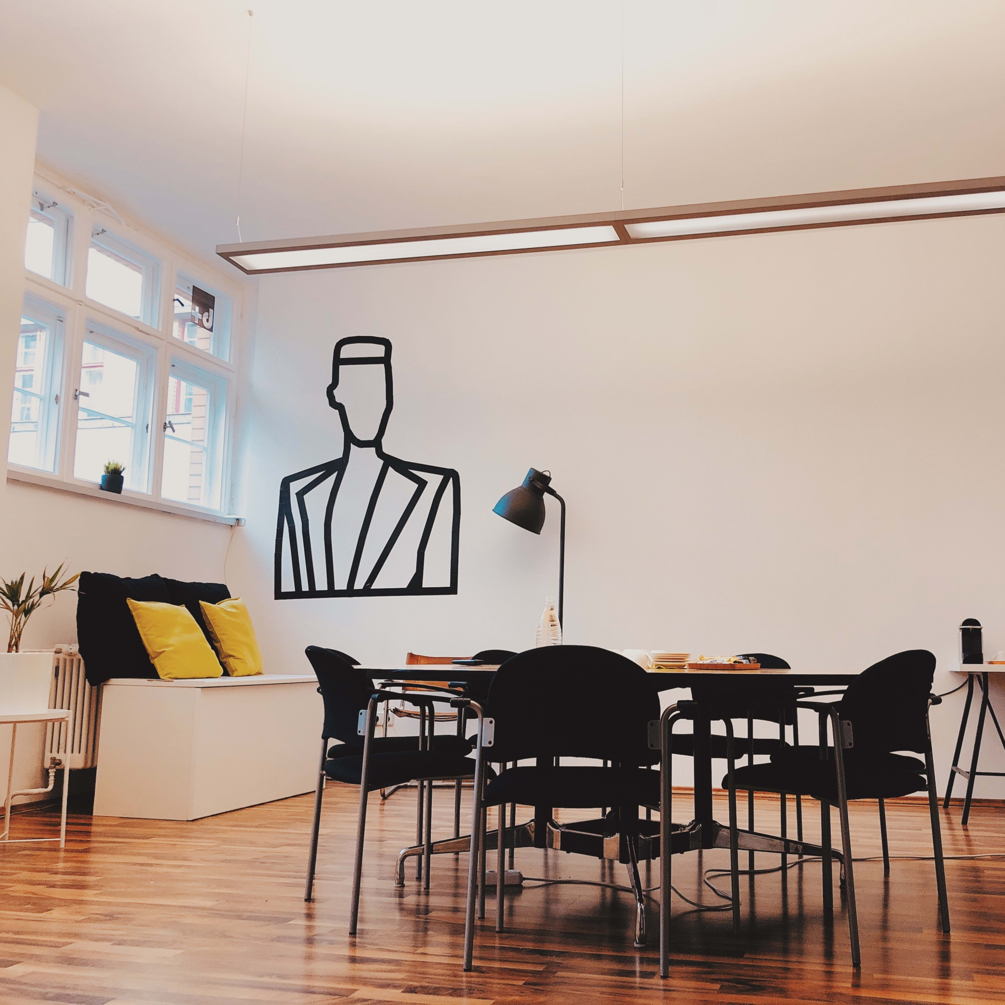 A dining area features a large wall mural of a person, a table with black chairs, and a sideboard displaying drinks and snacks.