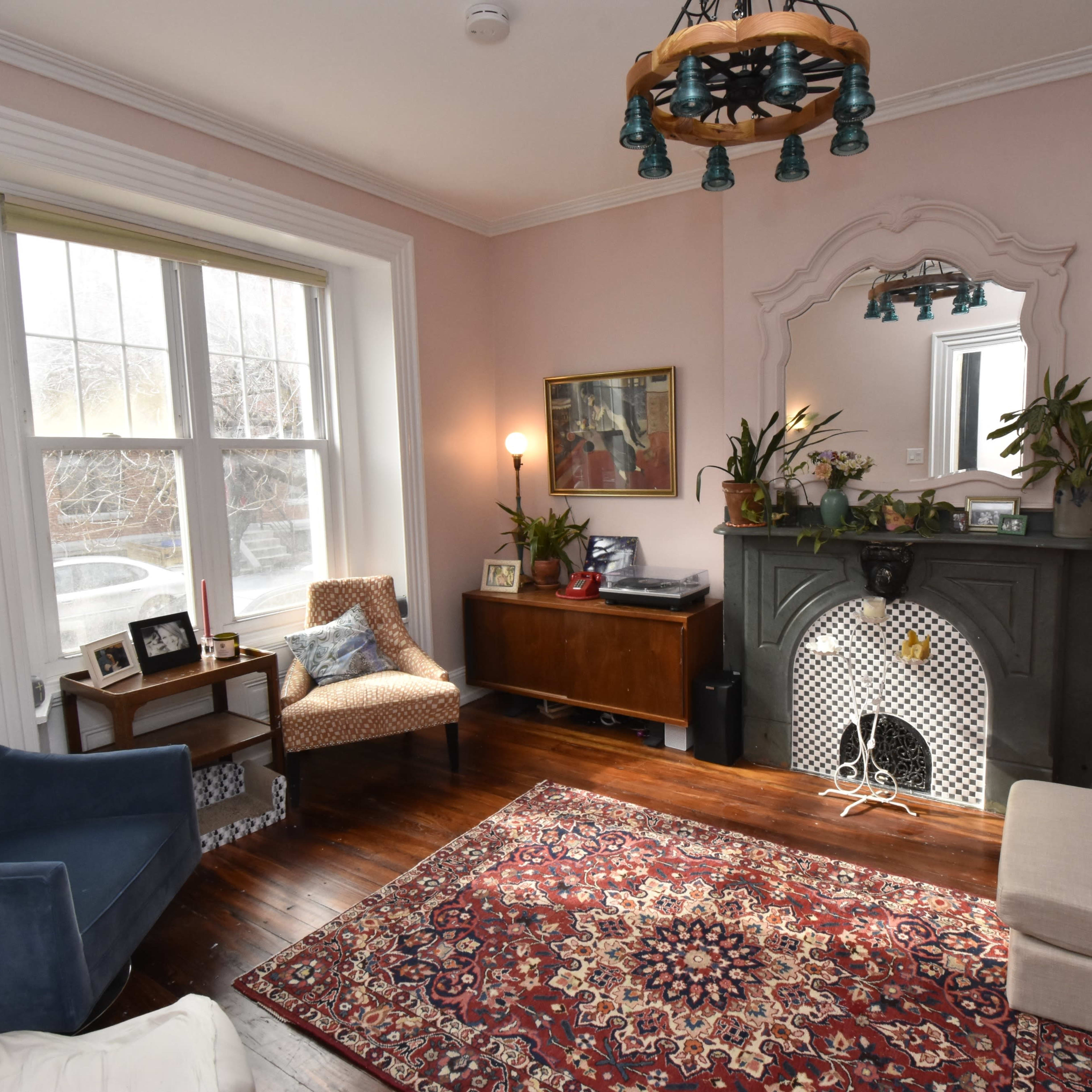 A cozy living room featuring a dark green fireplace, a beige sofa, a blue armchair, and a patterned rug on wooden floors.