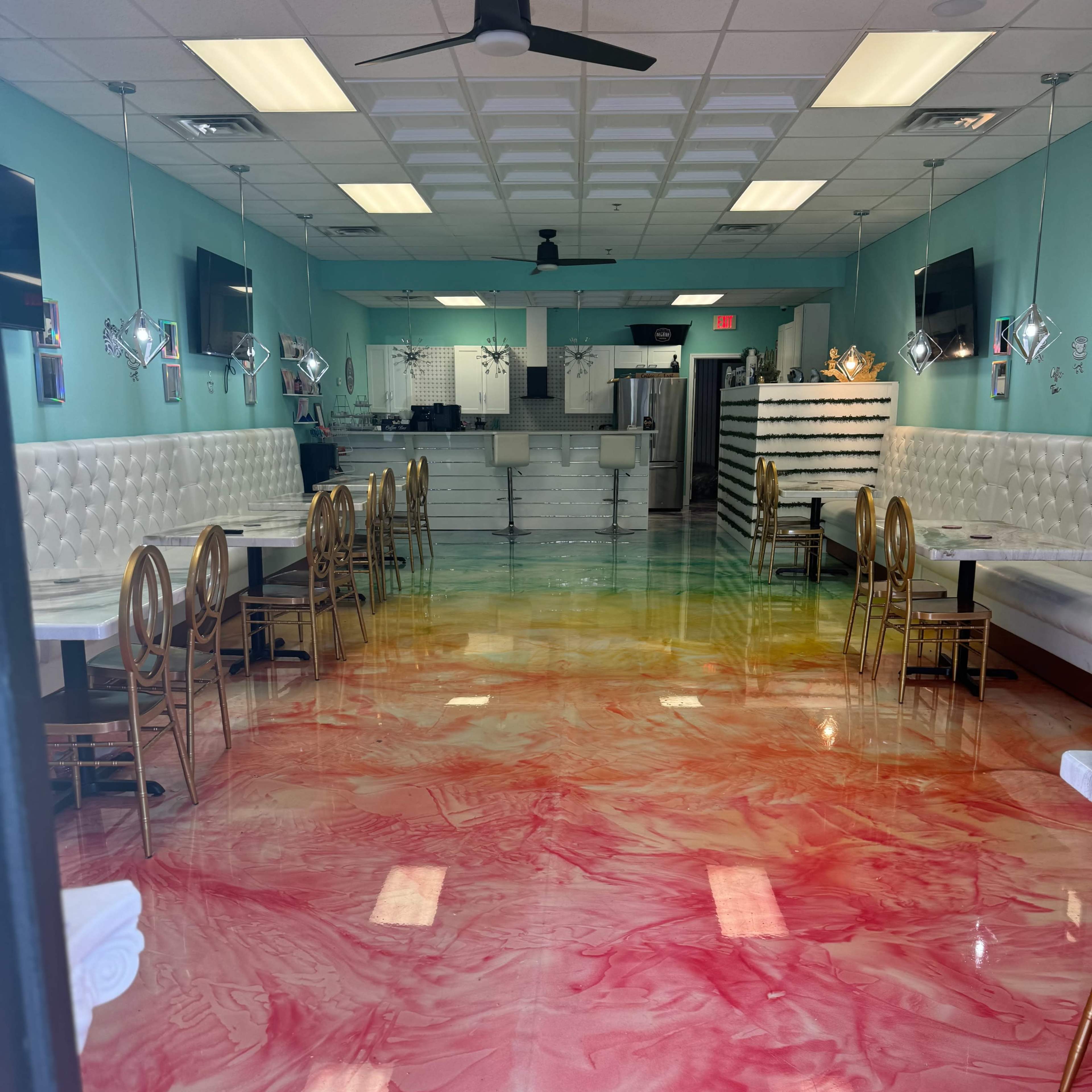 A colorful interior of a dessert shop, featuring a marbled pink and yellow floor, white leather seating, and modern decor with wall-mounted televisions.