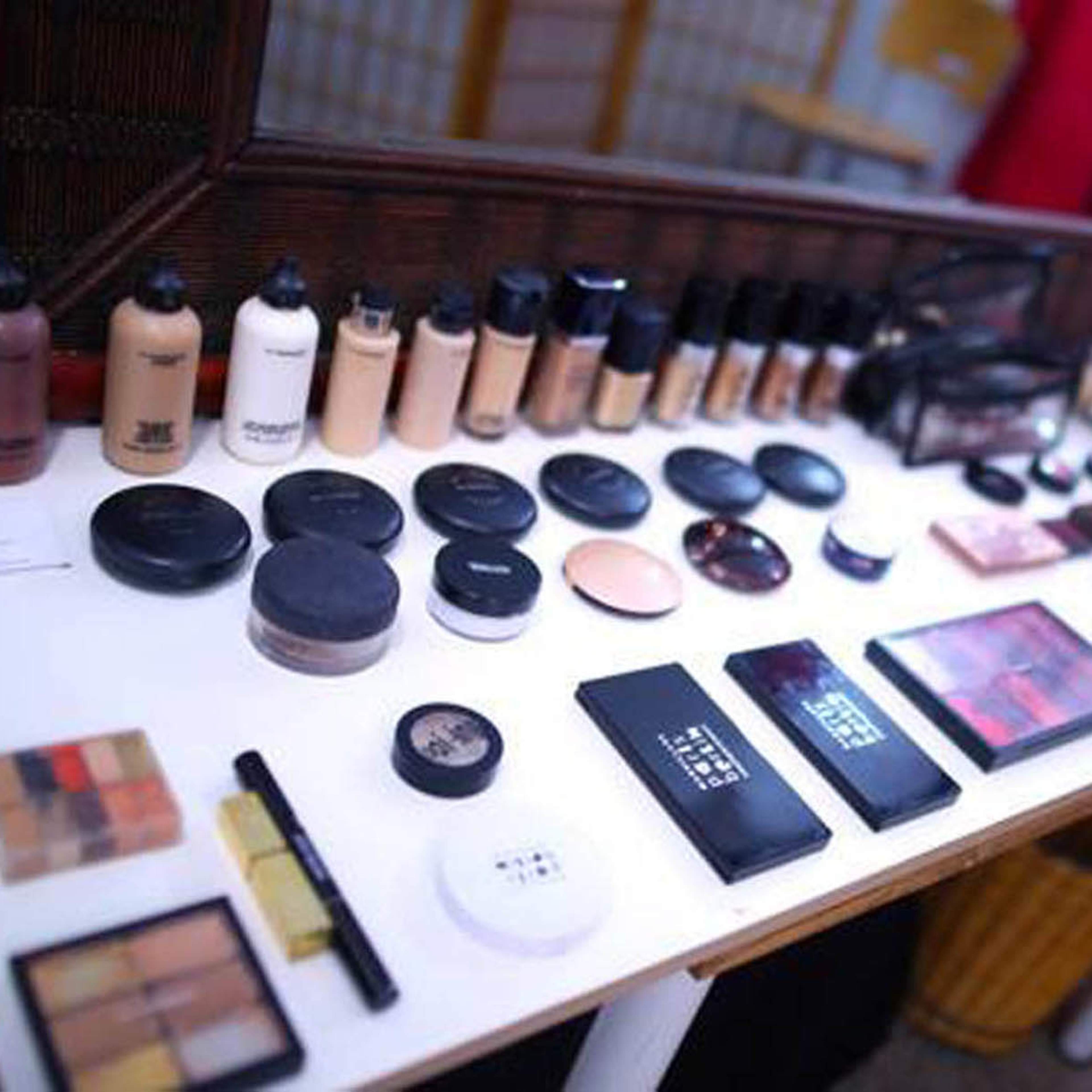 A table displays a variety of makeup products, including foundations, powders, and palettes, organized neatly in front of a mirror.