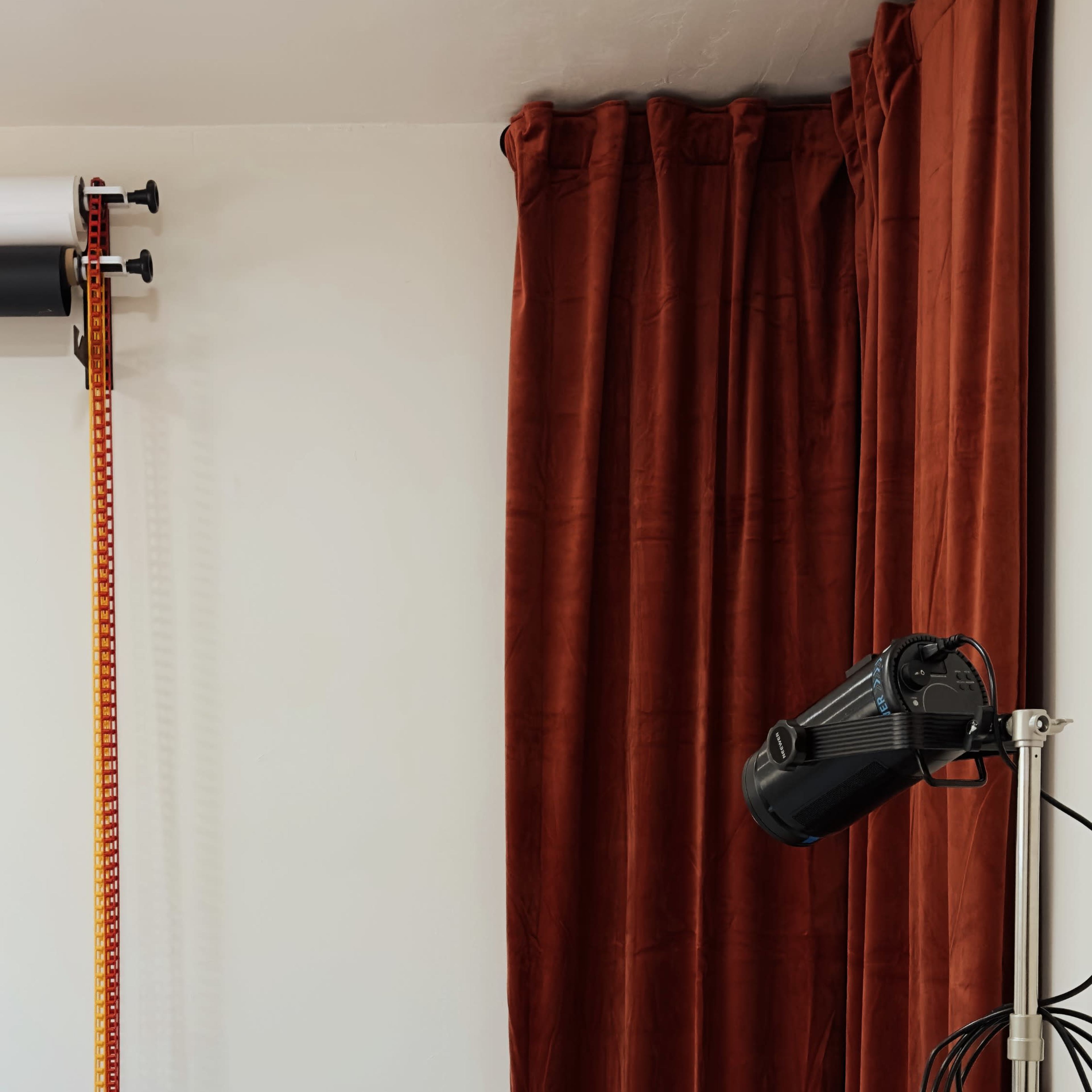 A room with a wall-mounted device, a curtain, and a floor lamp with multiple cords on a dark surface.