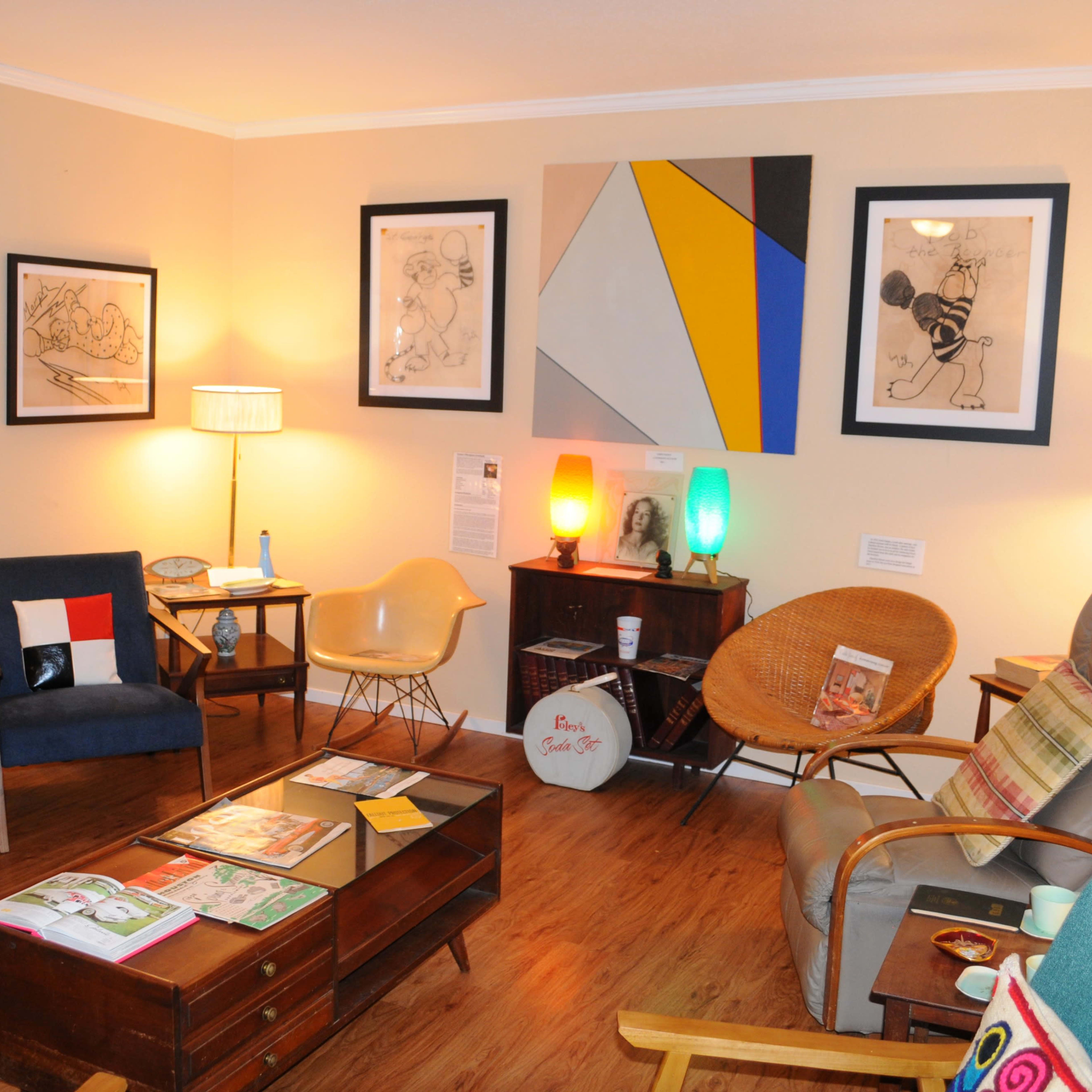 A cozy living room with various seating arrangements, colorful artwork on the walls, and a wooden coffee table topped with magazines.