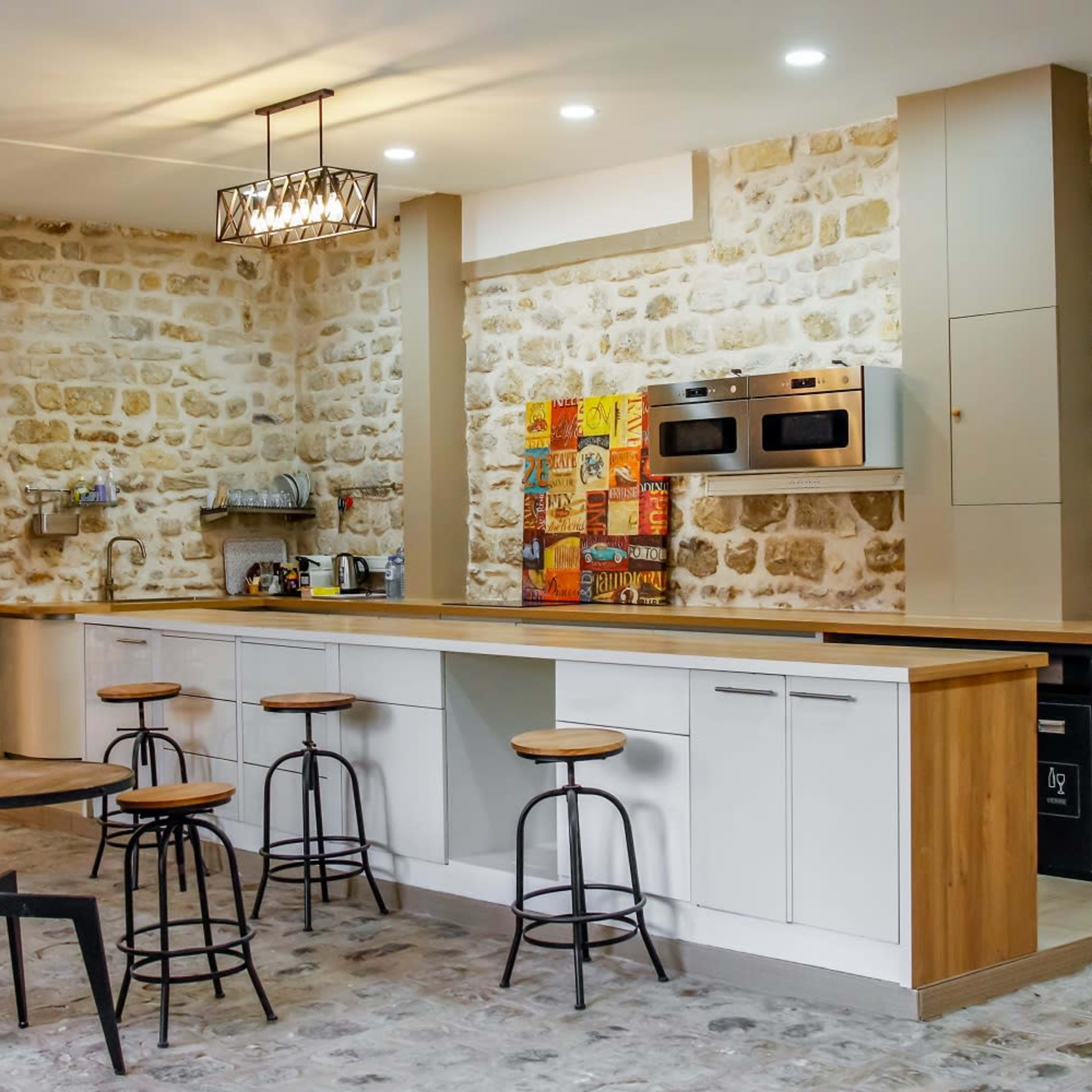 A modern kitchen with a stone wall, a wooden countertop, and several bar stools arranged in front.
