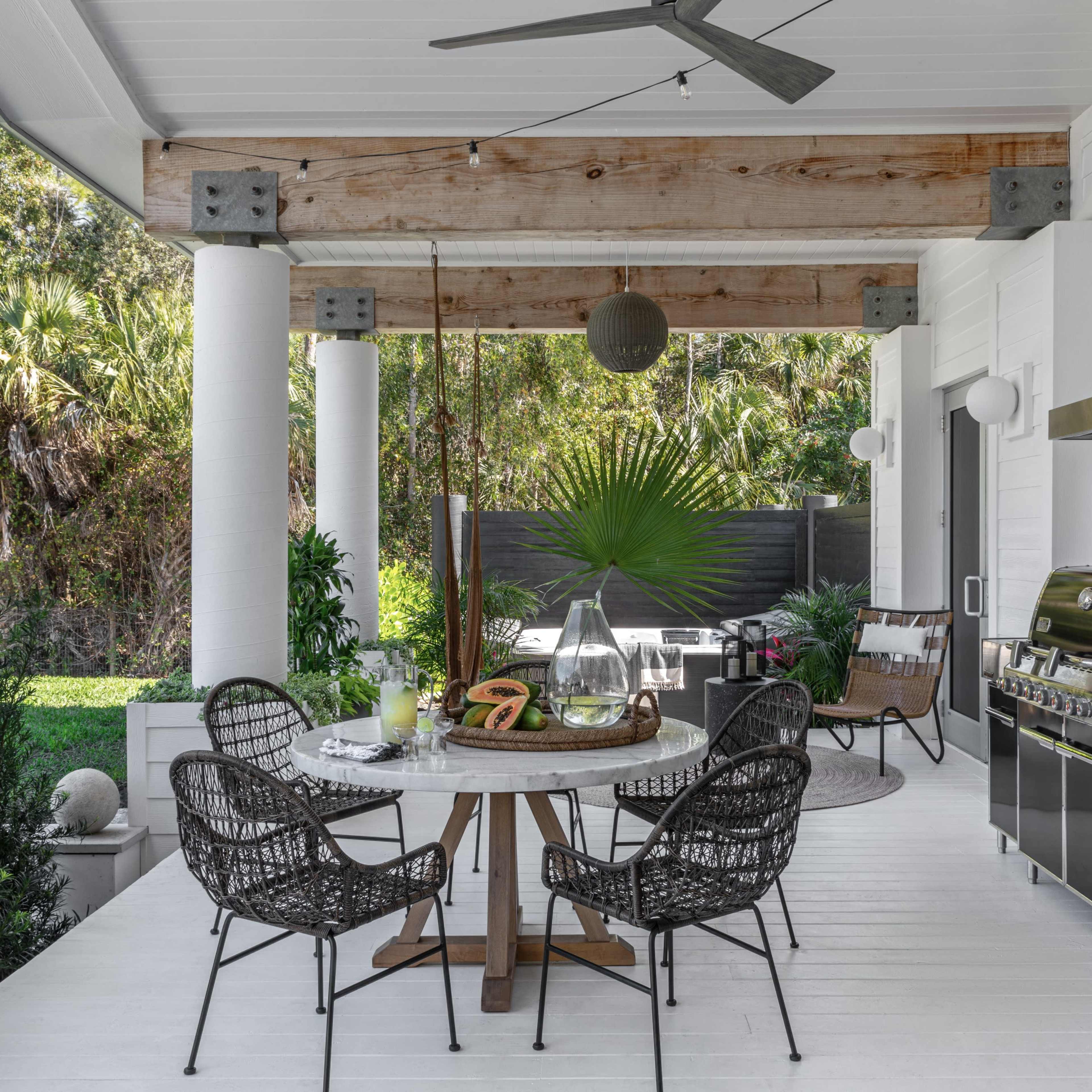 A modern outdoor kitchen and dining area featuring a circular table with chairs, a grill, and various plants in a lush backyard setting.
