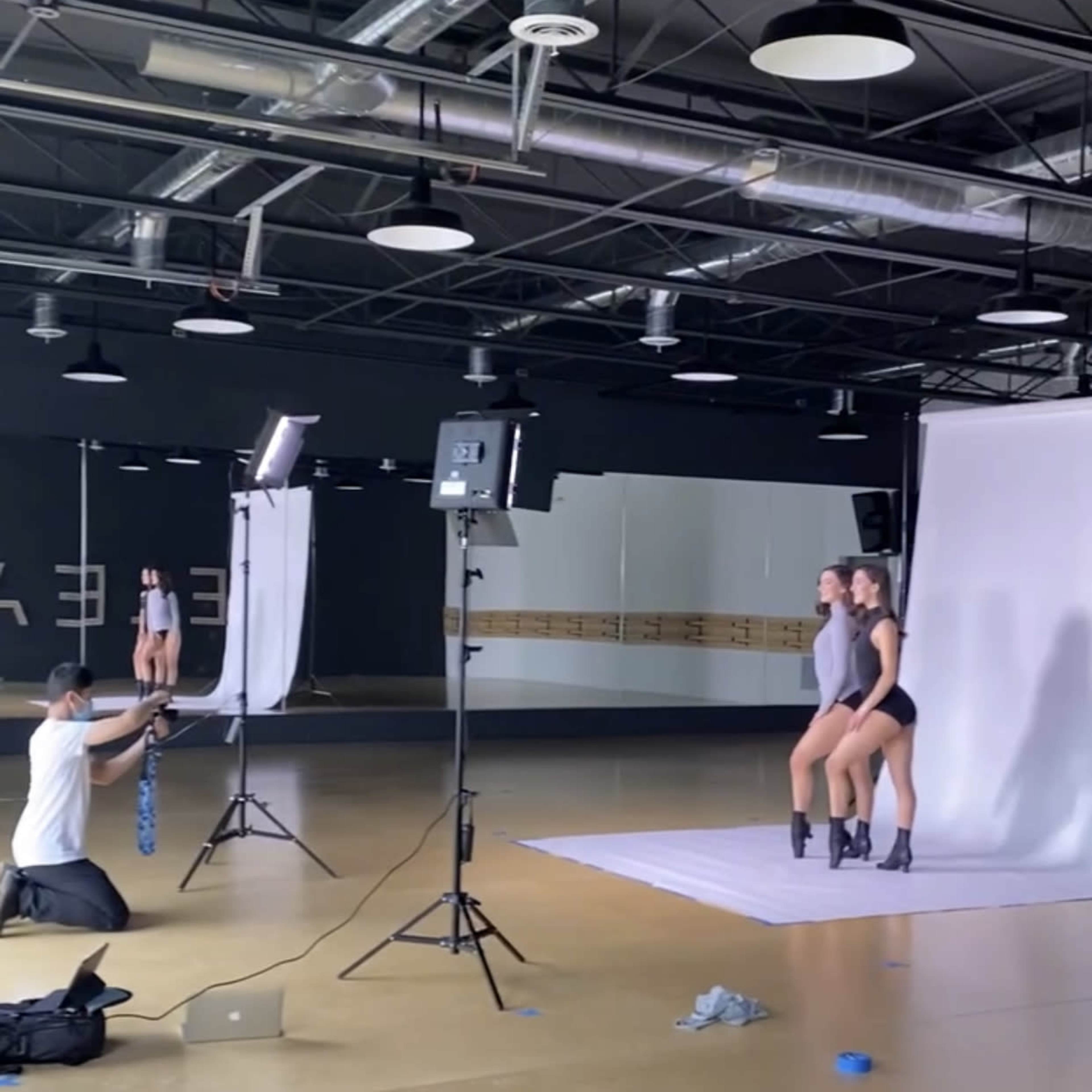 A photographer takes pictures of two models posing together in a studio with multiple lighting setups.