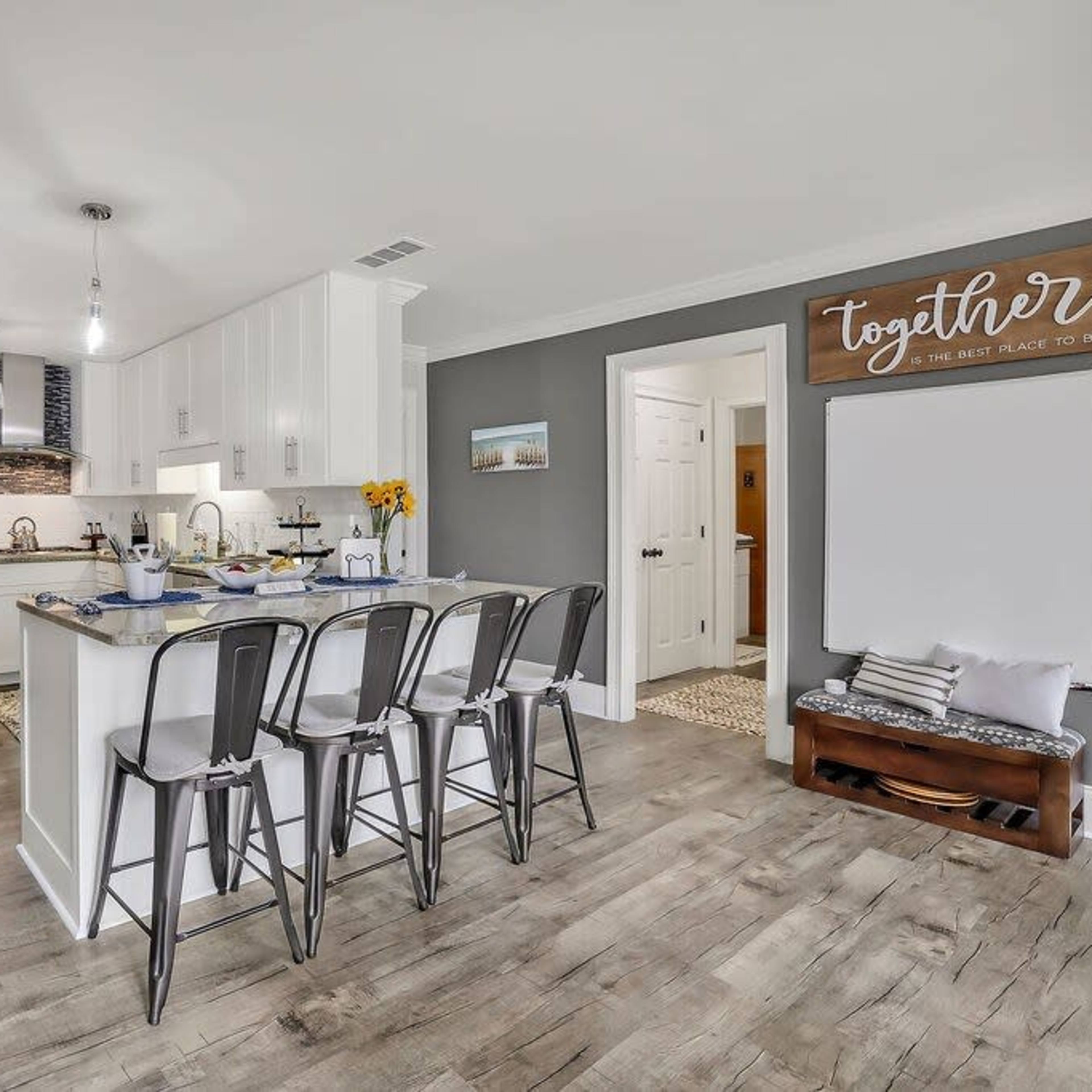 A modern kitchen features a central island with bar stools, white cabinetry, and a dining area in the background.