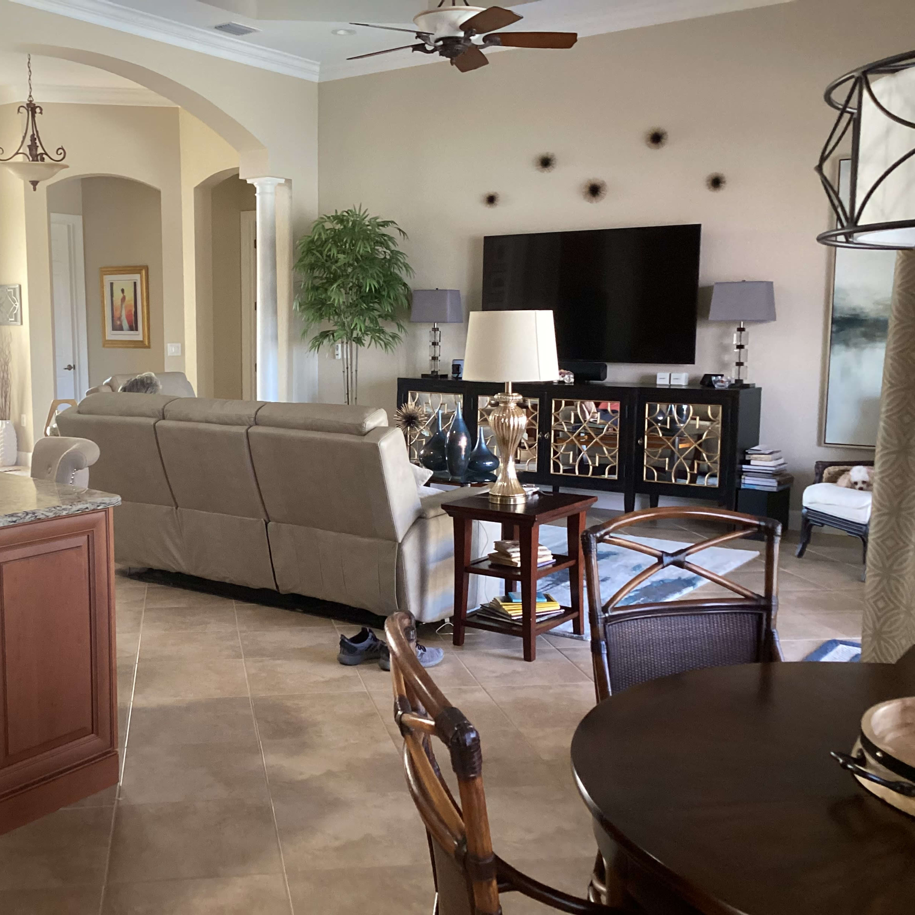 A spacious living area with a kitchen counter, a beige sofa facing a television, and a dining table with wicker chairs.