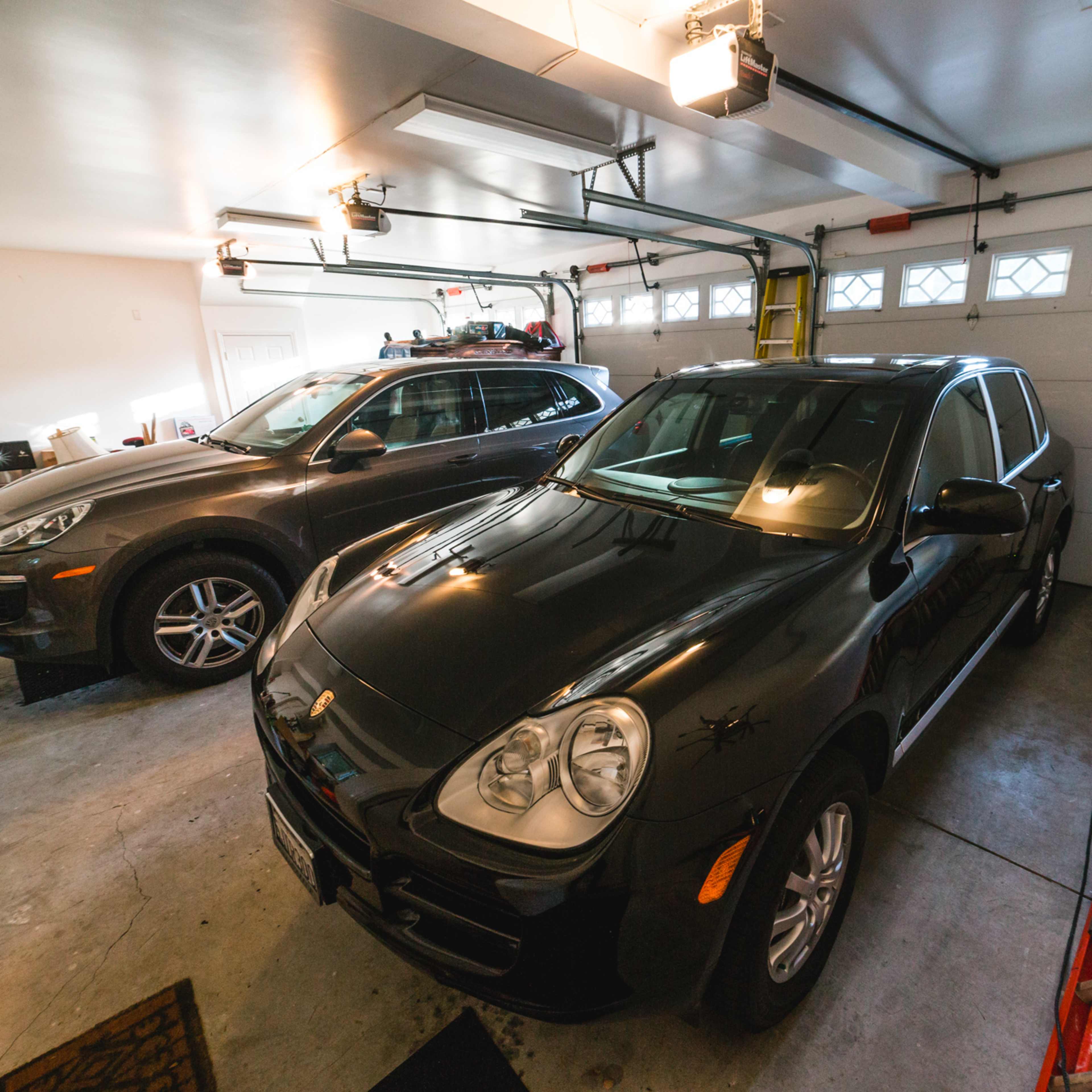 A black SUV and a gray crossover are parked in a residential garage with tools and equipment visible in the background.