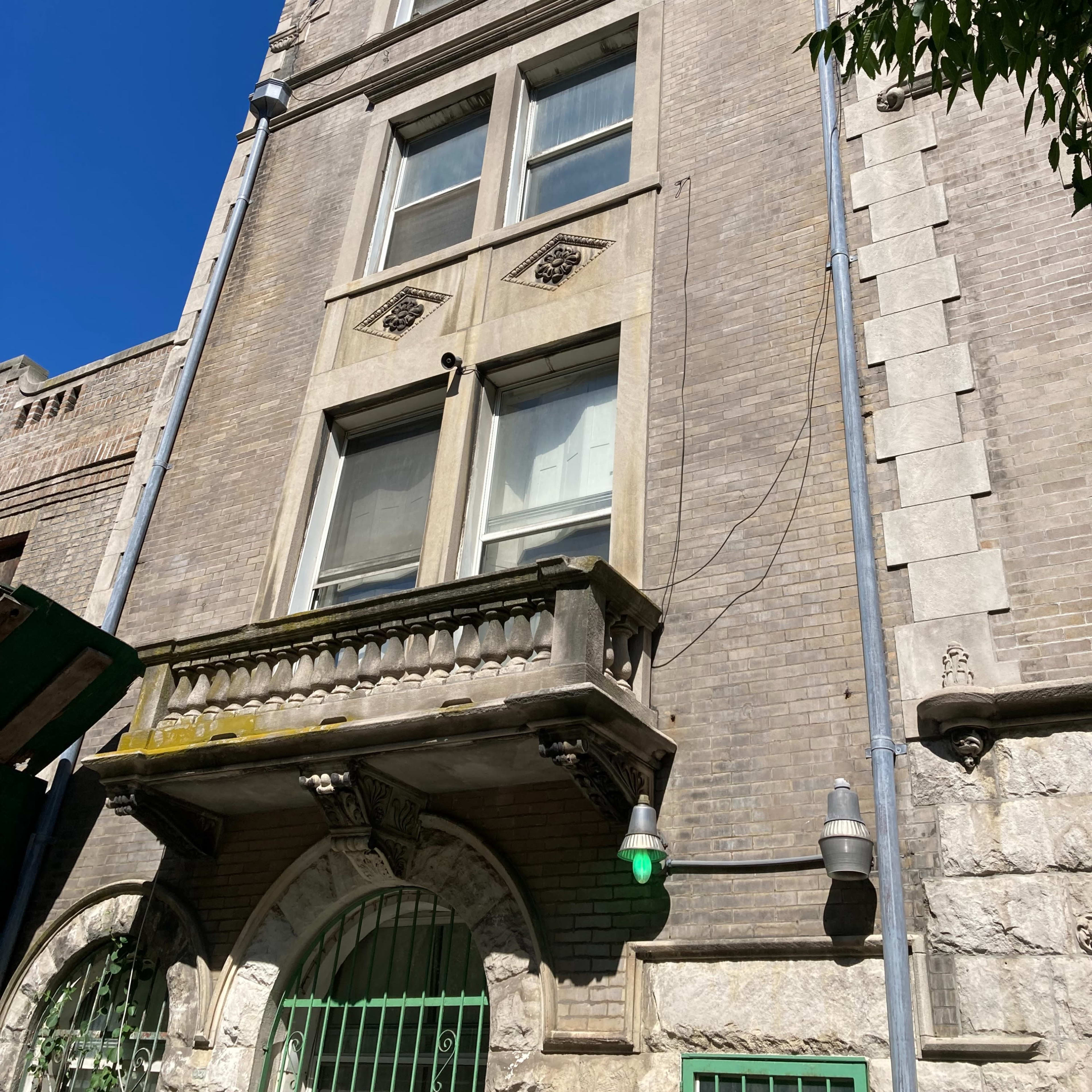 A tall, historic brick building with a peaked roof, multiple windows, and a balcony.