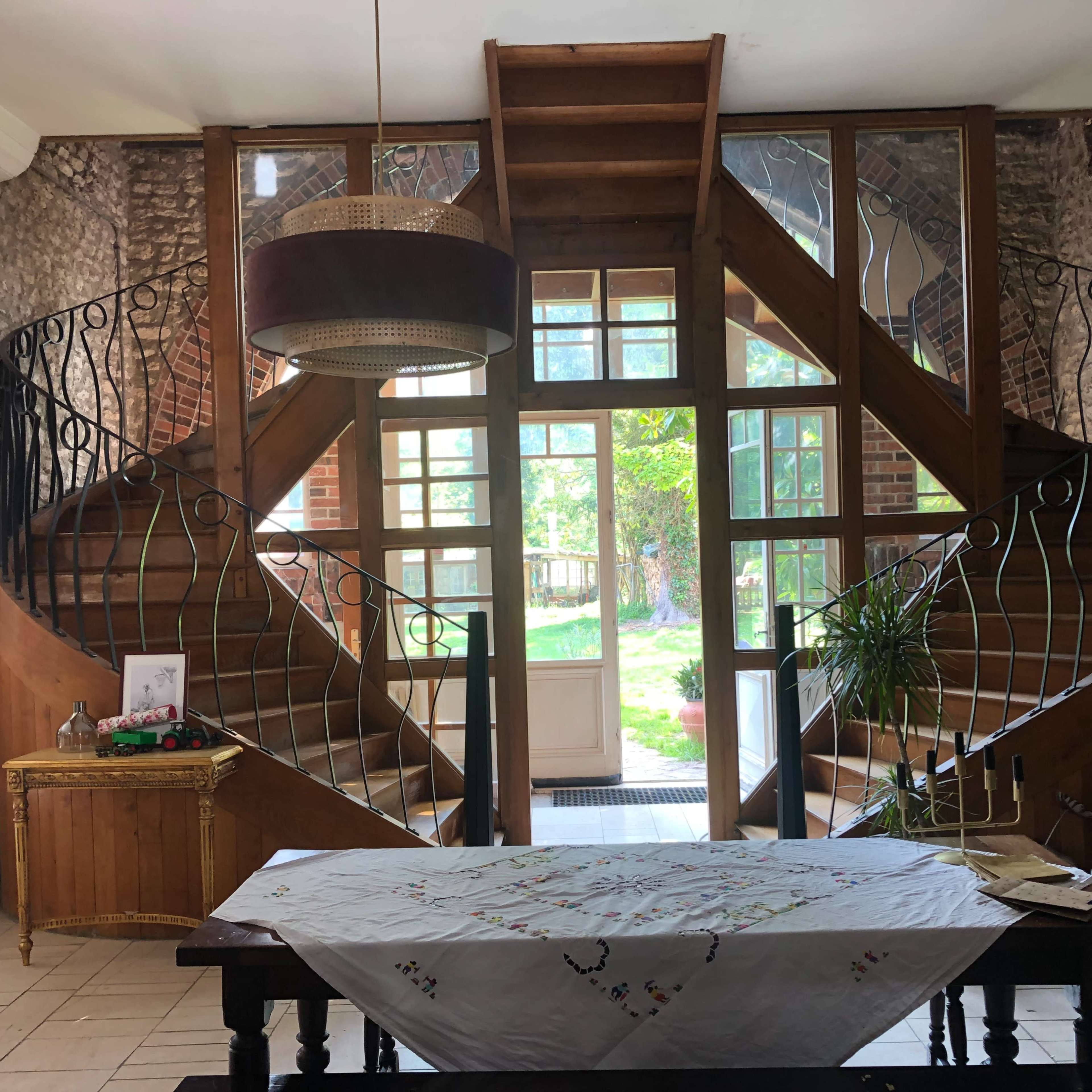 An interior entrance featuring a wooden staircase with intricate railings, flanked by large windows that illuminate the space.