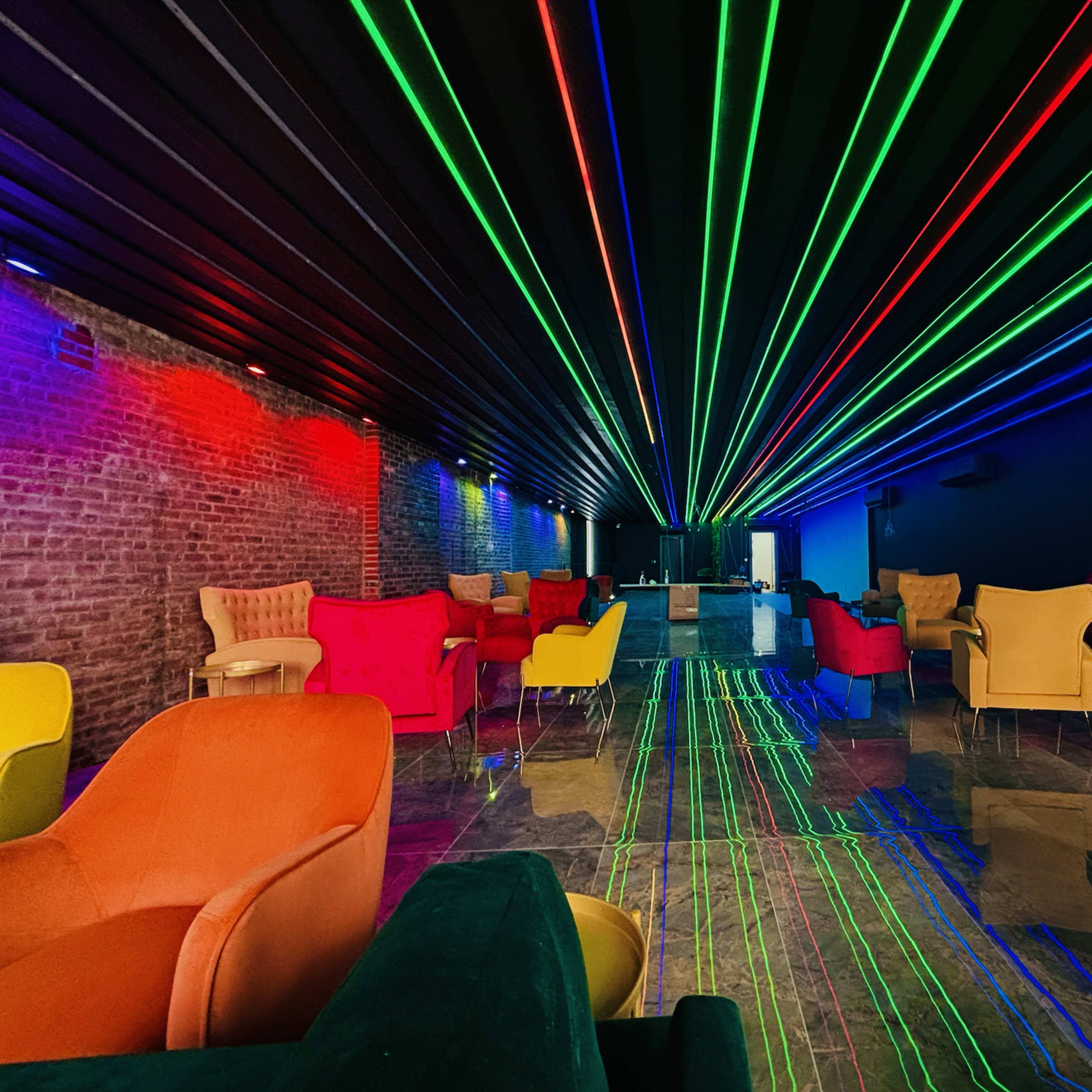 A modern lounge with colorful furniture and vibrant laser beams projecting from the ceiling.