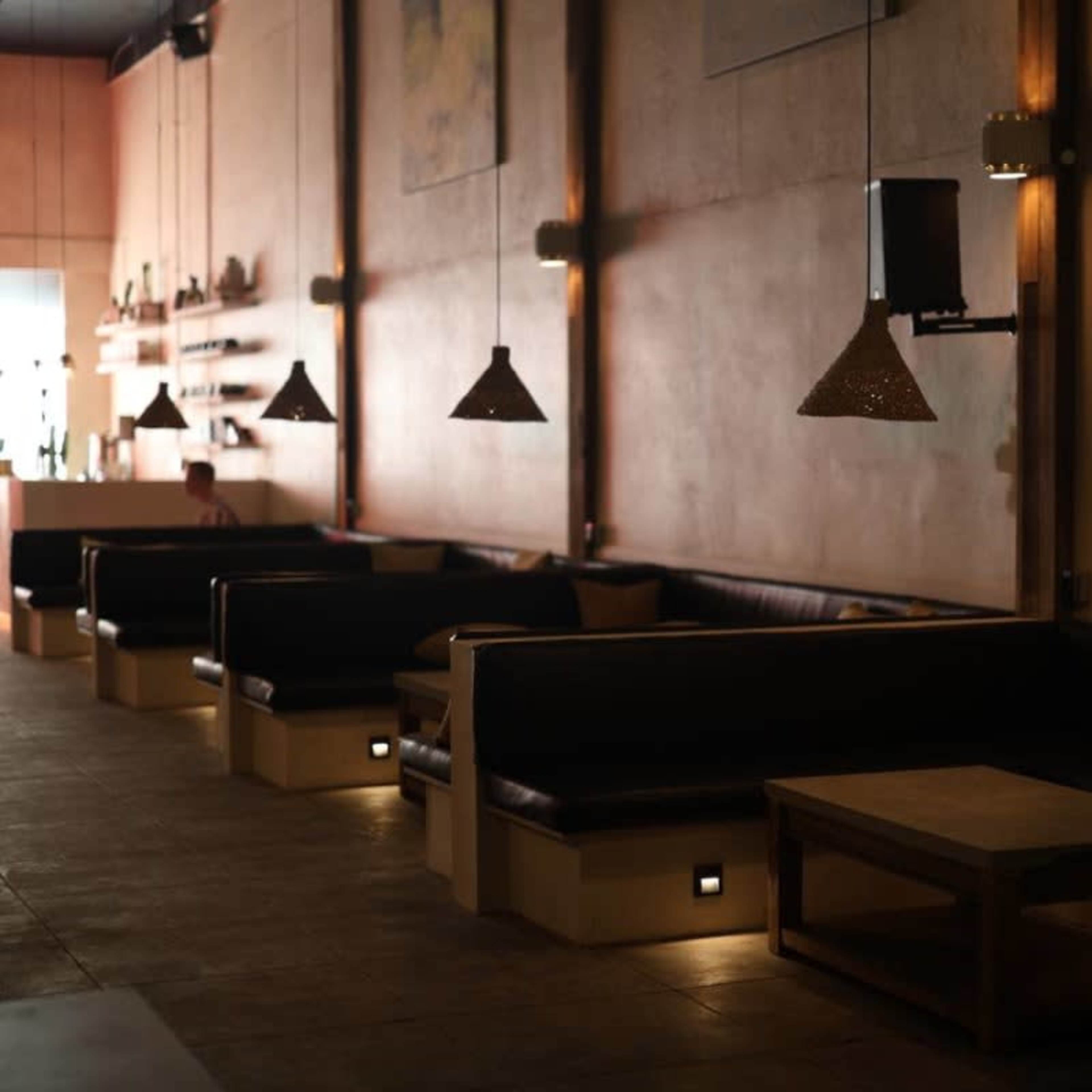 A dimly lit café interior with black leather seating and wooden tables along a textured wall.