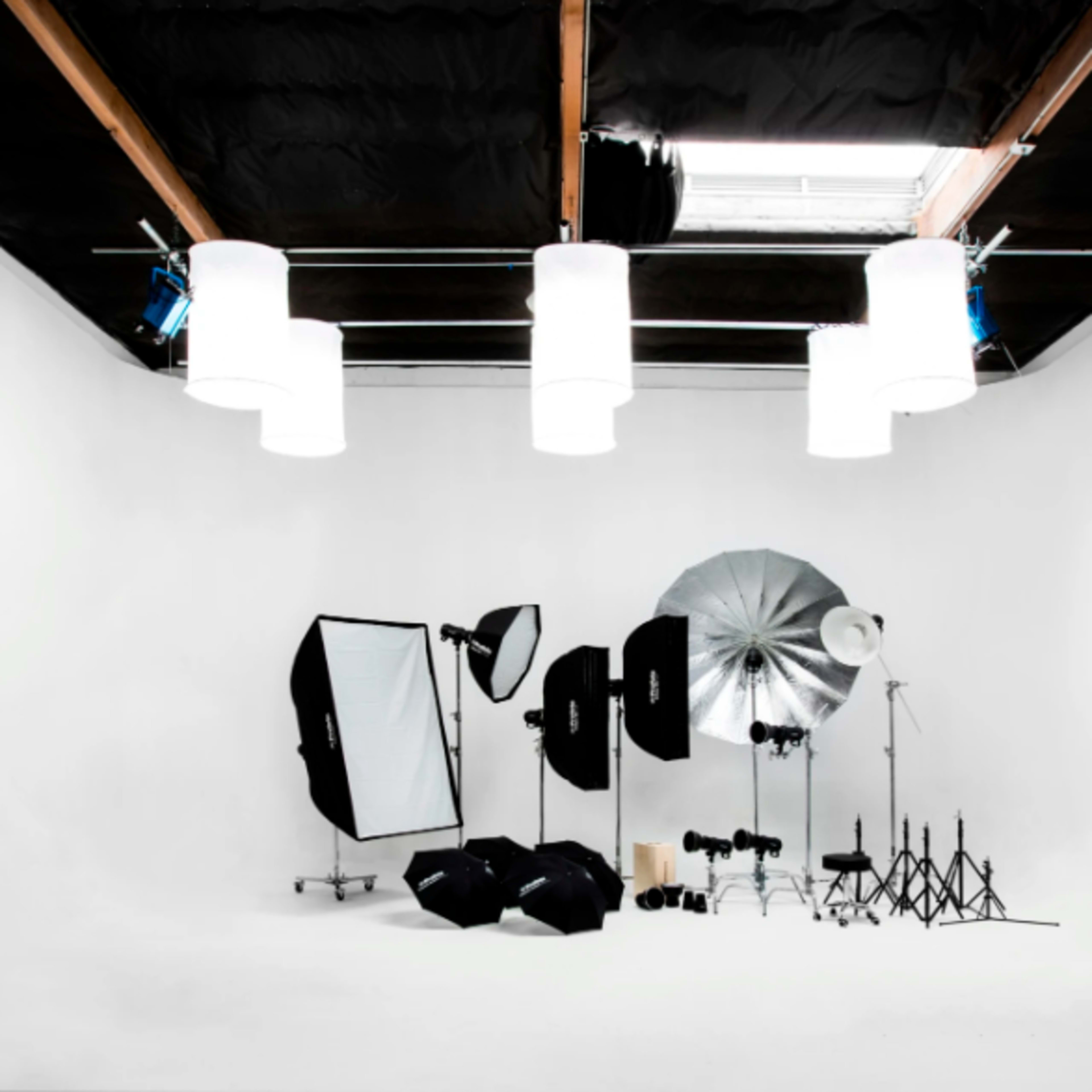 A photography studio with a white backdrop, lighting equipment, reflectors, and stands arranged in the space.