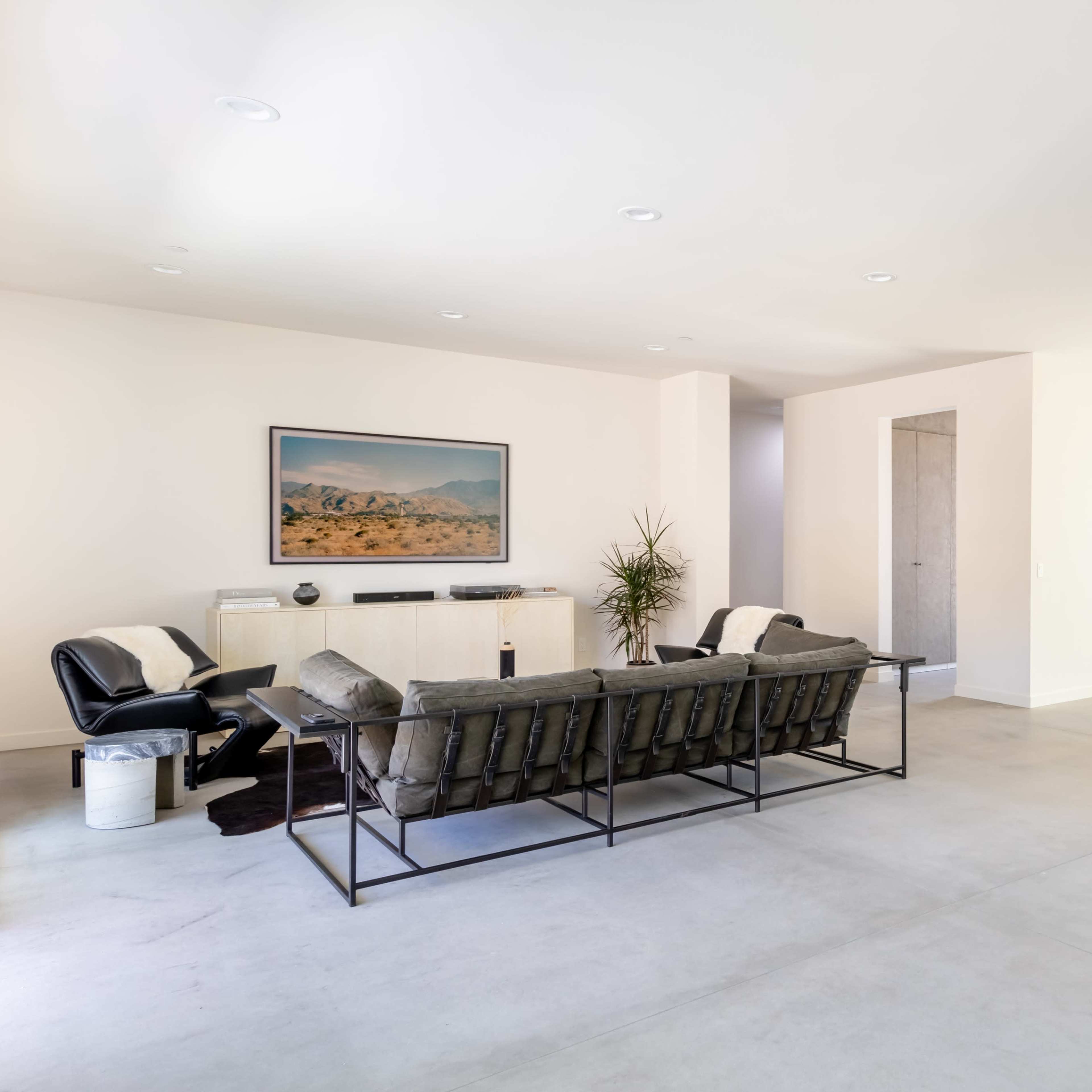 A modern living room with minimalist furniture, a large window, and a dining area adjacent to it.