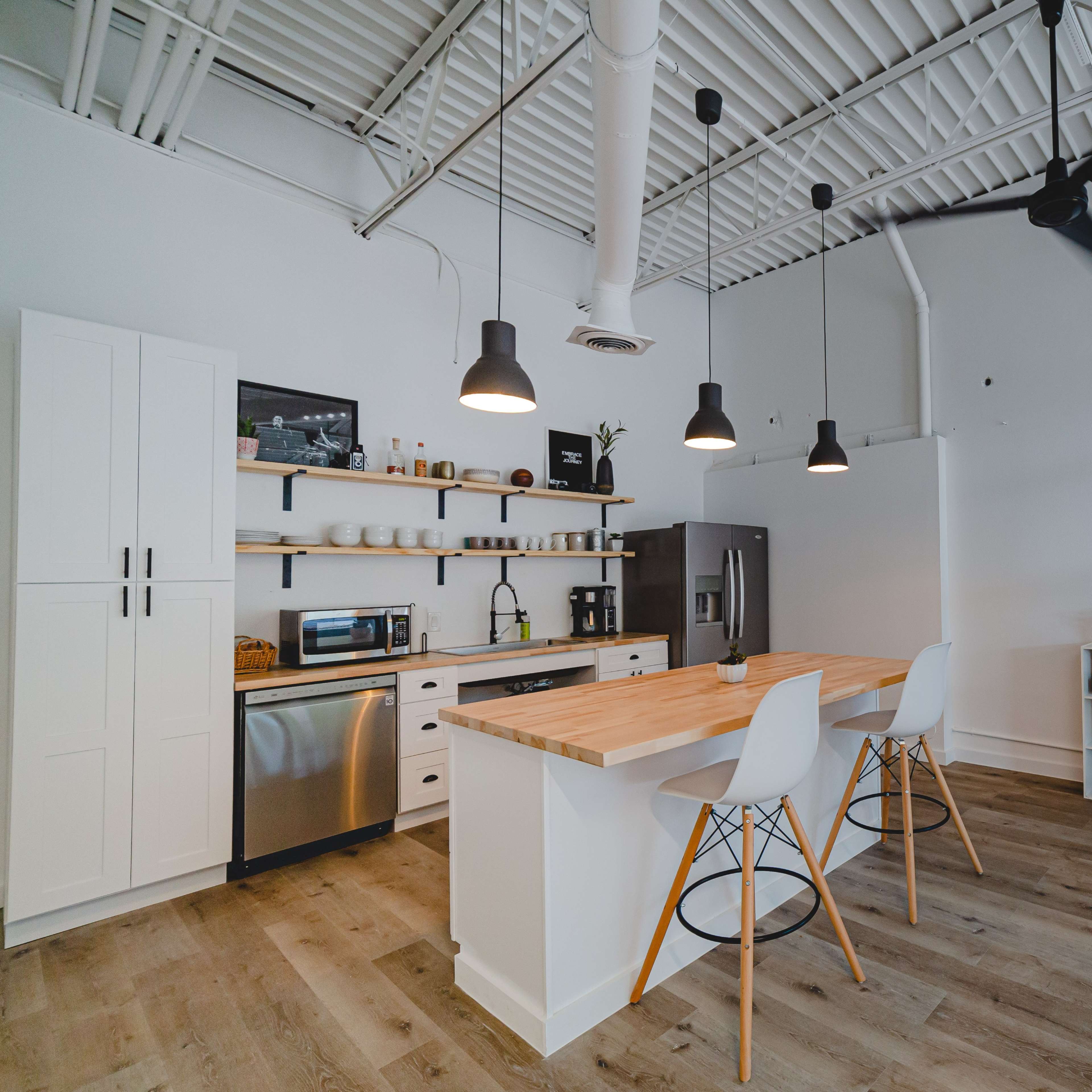 A modern kitchen features a large island with seating, stainless steel appliances, and open shelving against a white backdrop.
