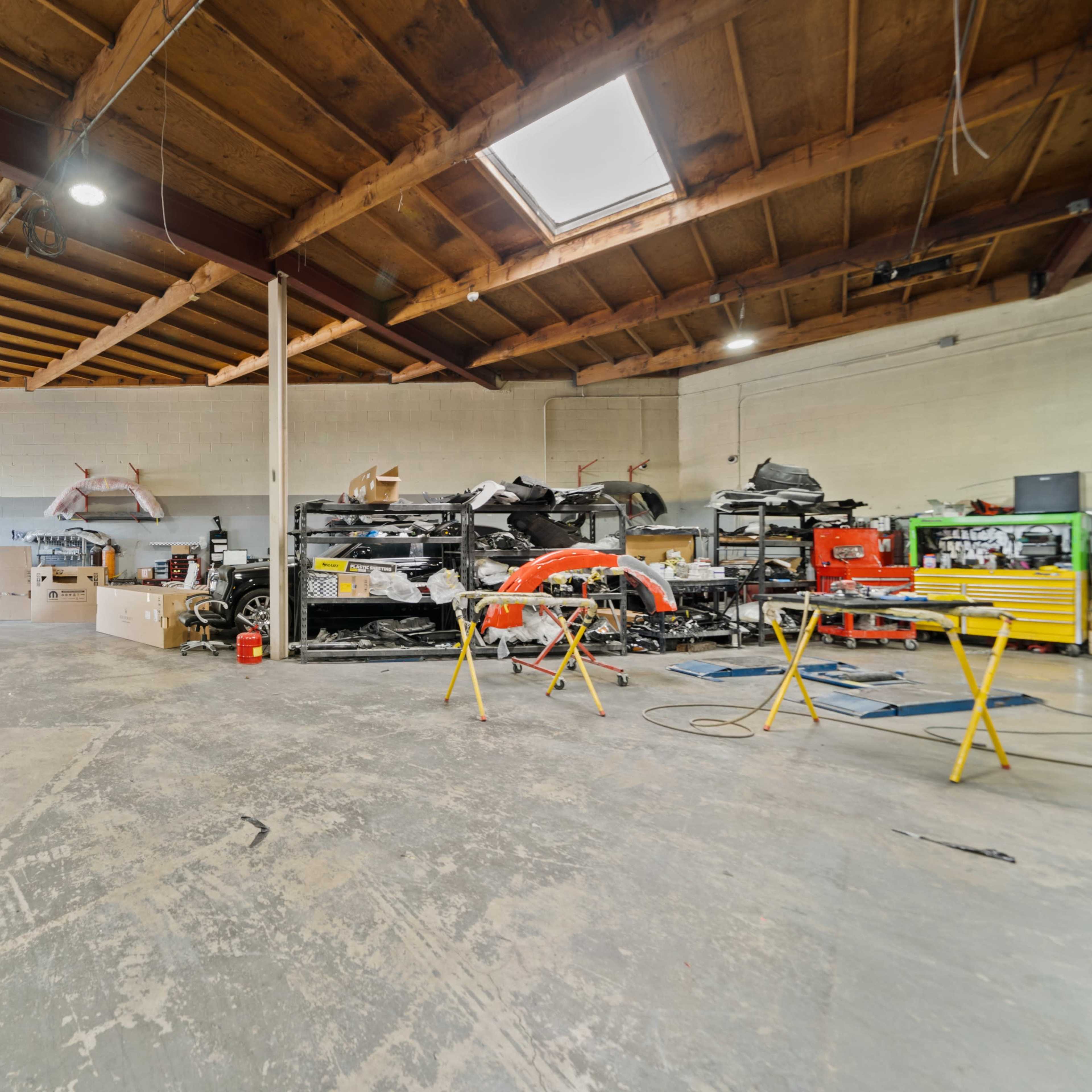 A spacious garage with various tools and materials organized around the area, including several cars and workbenches.
