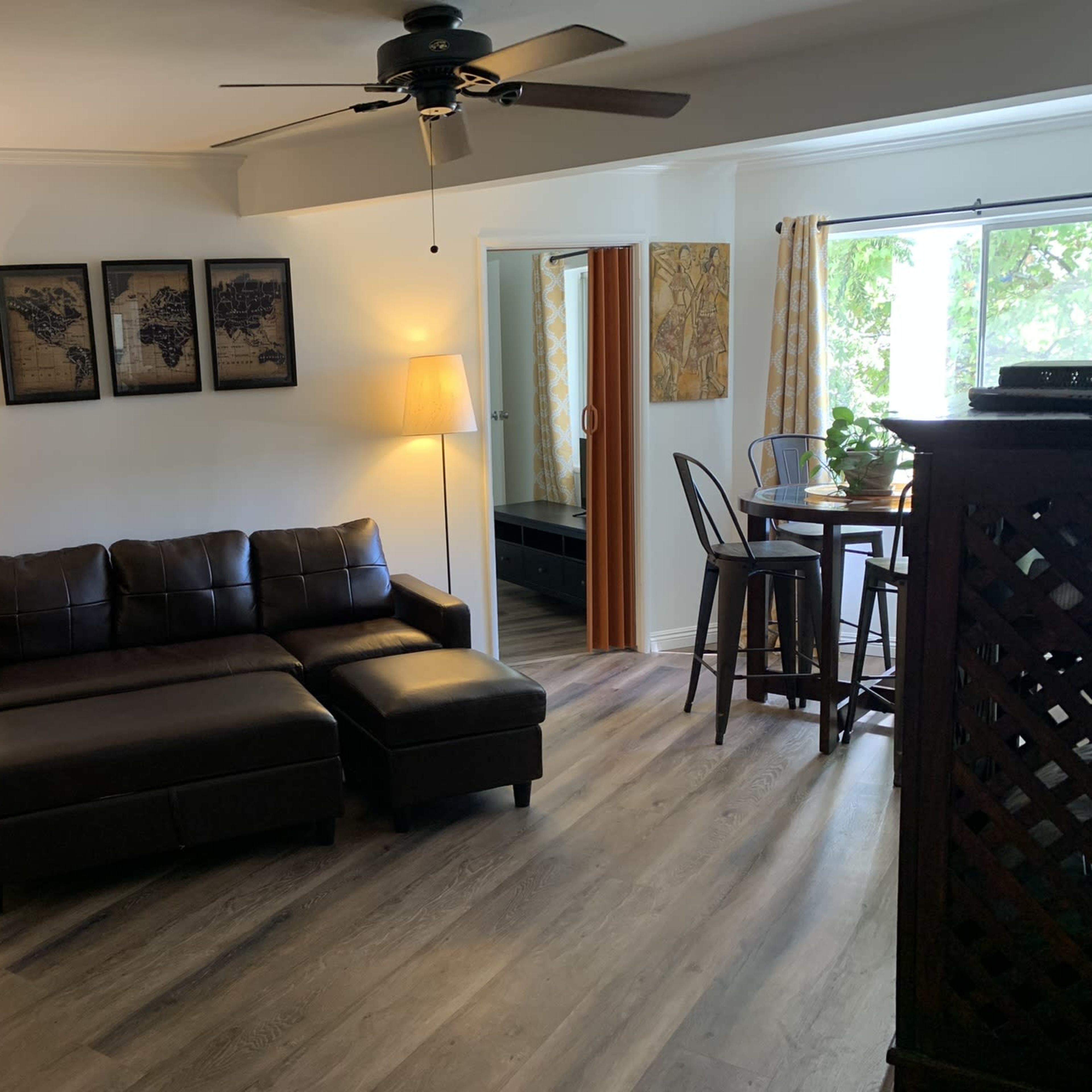 A modern living space with a dark brown sectional sofa, a small dining table, and a floor lamp, all set against light-colored walls and wooden flooring.