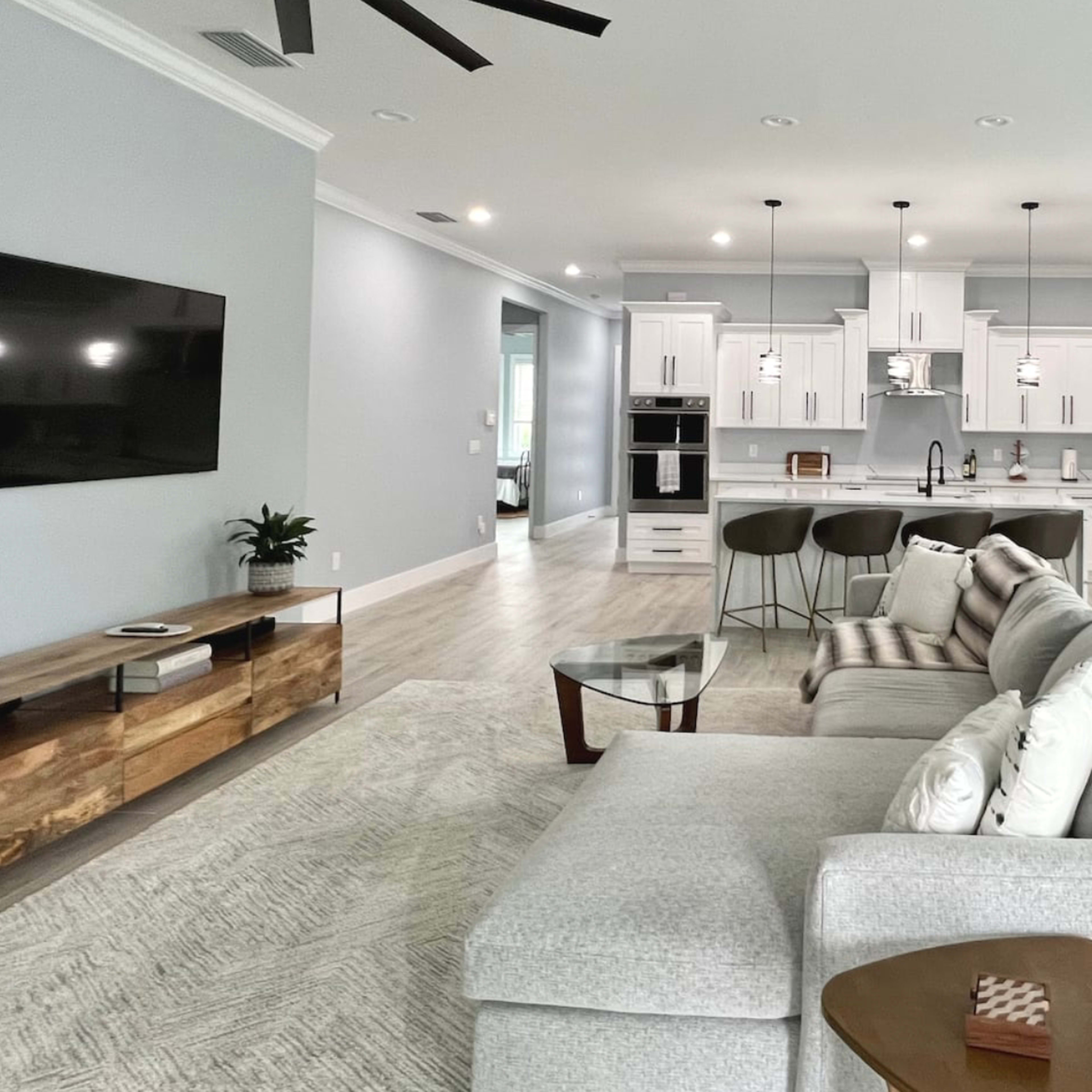 A modern, open-concept living space with a gray and white color scheme, featuring a sectional sofa, a kitchen with an island, and a dining area.